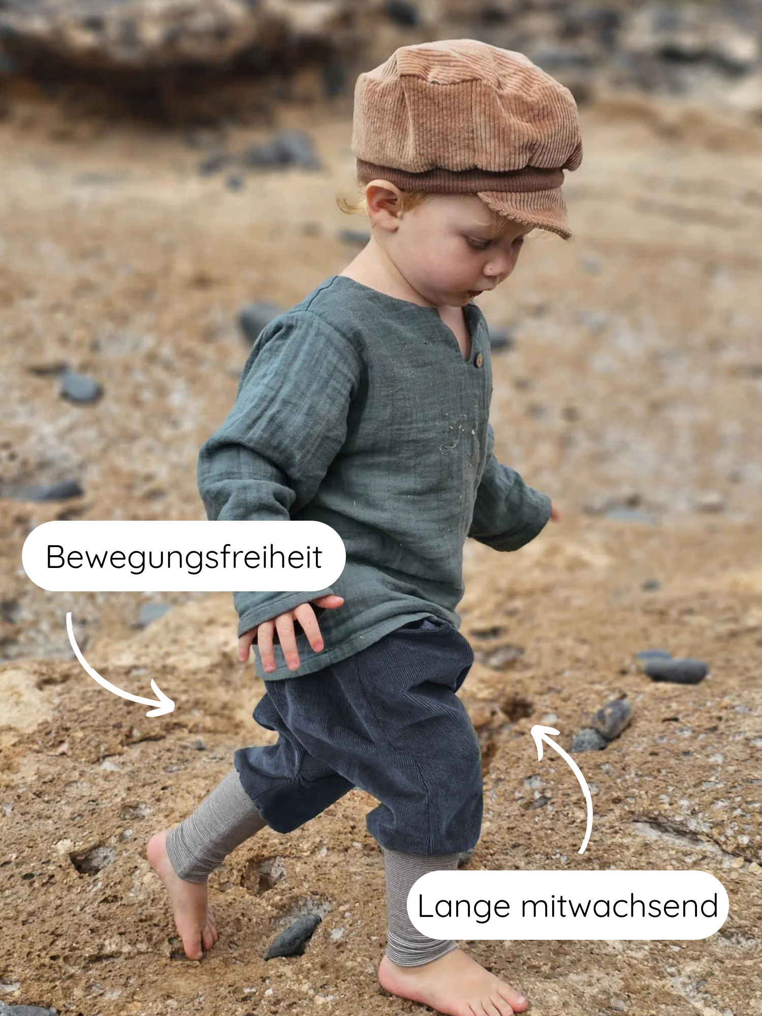 Kleinkind barfuß am Strand in Knickerbocker Feincord Ringel - Blaubeere, mit lockerer Passform für Bewegungsfreiheit und mitwachsendem Design. Trägt moosgrünes Oberteil und braune Schiebermütze.