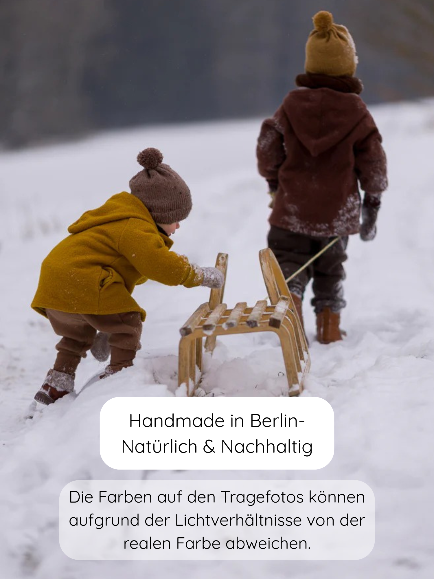 Zwei Kinder im Schnee mit einem Holzschlitten tragen die Winter Wichteljacke Wollwalk - Schoko, die durch ihre spitze Kapuze und breite Krempelbündchen auffällt, ideal für kalte Tage.