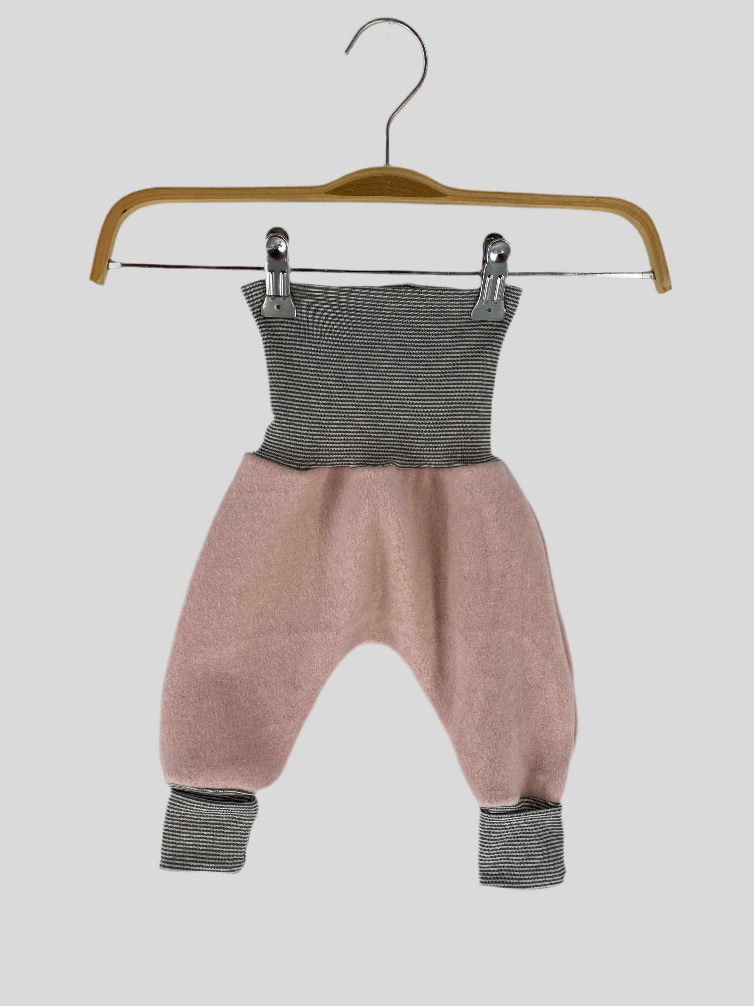 NEU Babyknicker Plüsch Puder mit Ringel Gr 3M hängt an einem Holzkleiderbügel, mit einem metallenen Clip befestigt, neben einem Paar Socken, auf einem Holzschwinger.