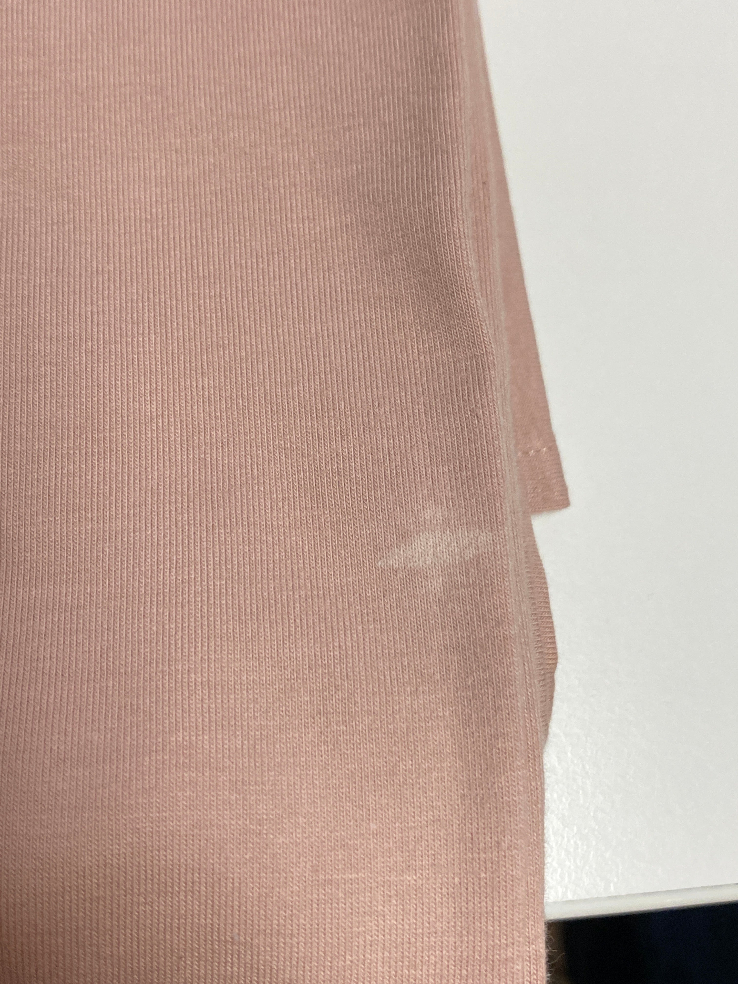 Nahaufnahme des Bleistiftrock Jersey Puder Gr. L, zeigt eine blassrosa, gerippte Struktur mit einem kleinen Fleck in der Mitte rechts, auf einer weißen Oberfläche liegend. Zustand: neu, kleine Flecken hinten.