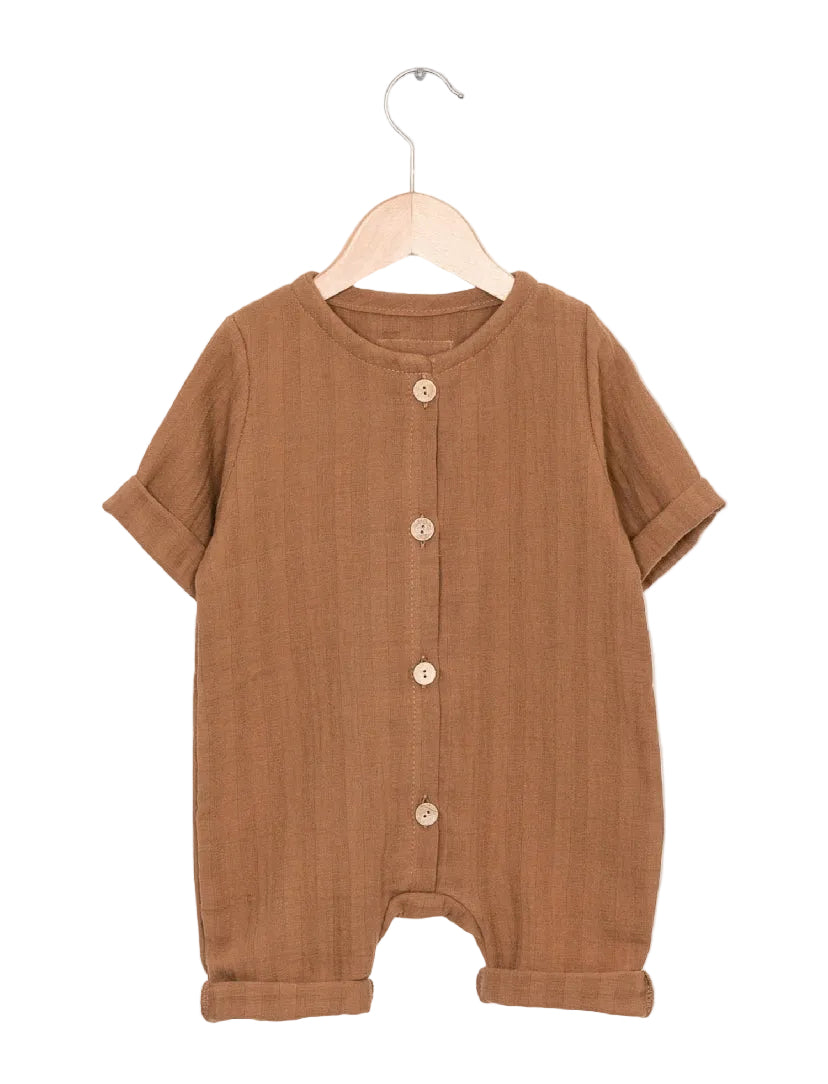 Mini Overall Musselin Sahara Gr 0M: Ein brauner, kurzärmeliger Baby-Strampler aus strukturiertem Stoff, mit Rundhalsausschnitt, Holzknöpfen vorne und umgeschlagenen Beinöffnungen, auf einem Holzkleiderbügel vor neutralem Hintergrund.