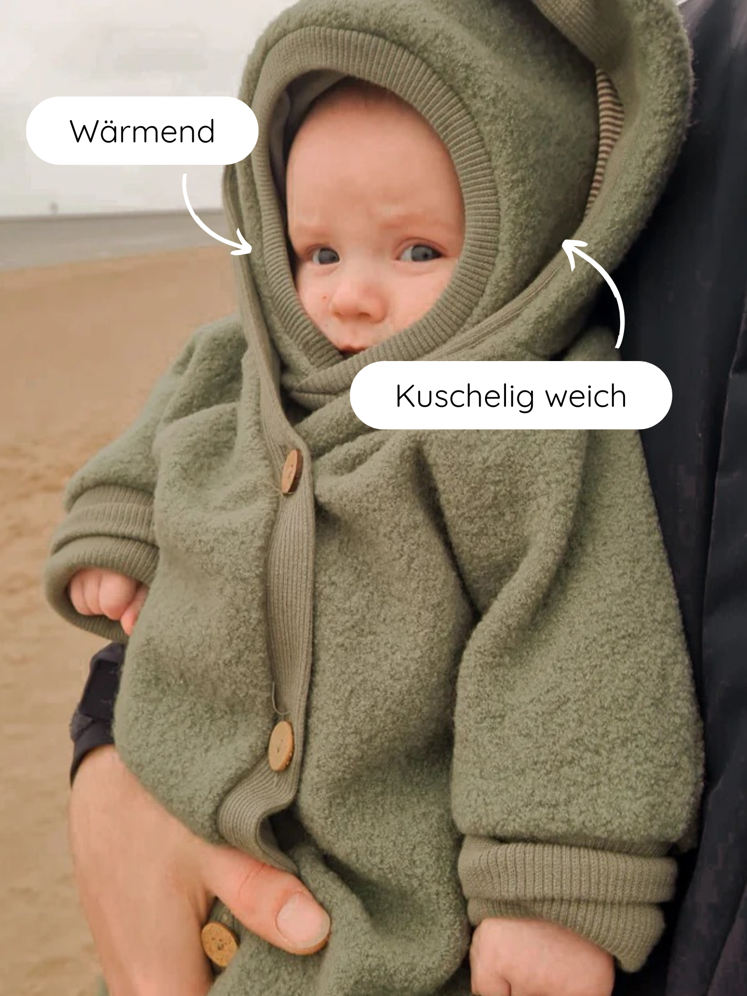 Ein Baby im weichen, olivgrünen Fleece-Einteiler mit Kapuze wird gehalten. Schlupfmütze Wollwalk - Pistazie schützt mit wärmendem, kuschelweichem Tragekomfort. Perfekt für kalte Tage, bleibt sicher an Ort und Stelle.