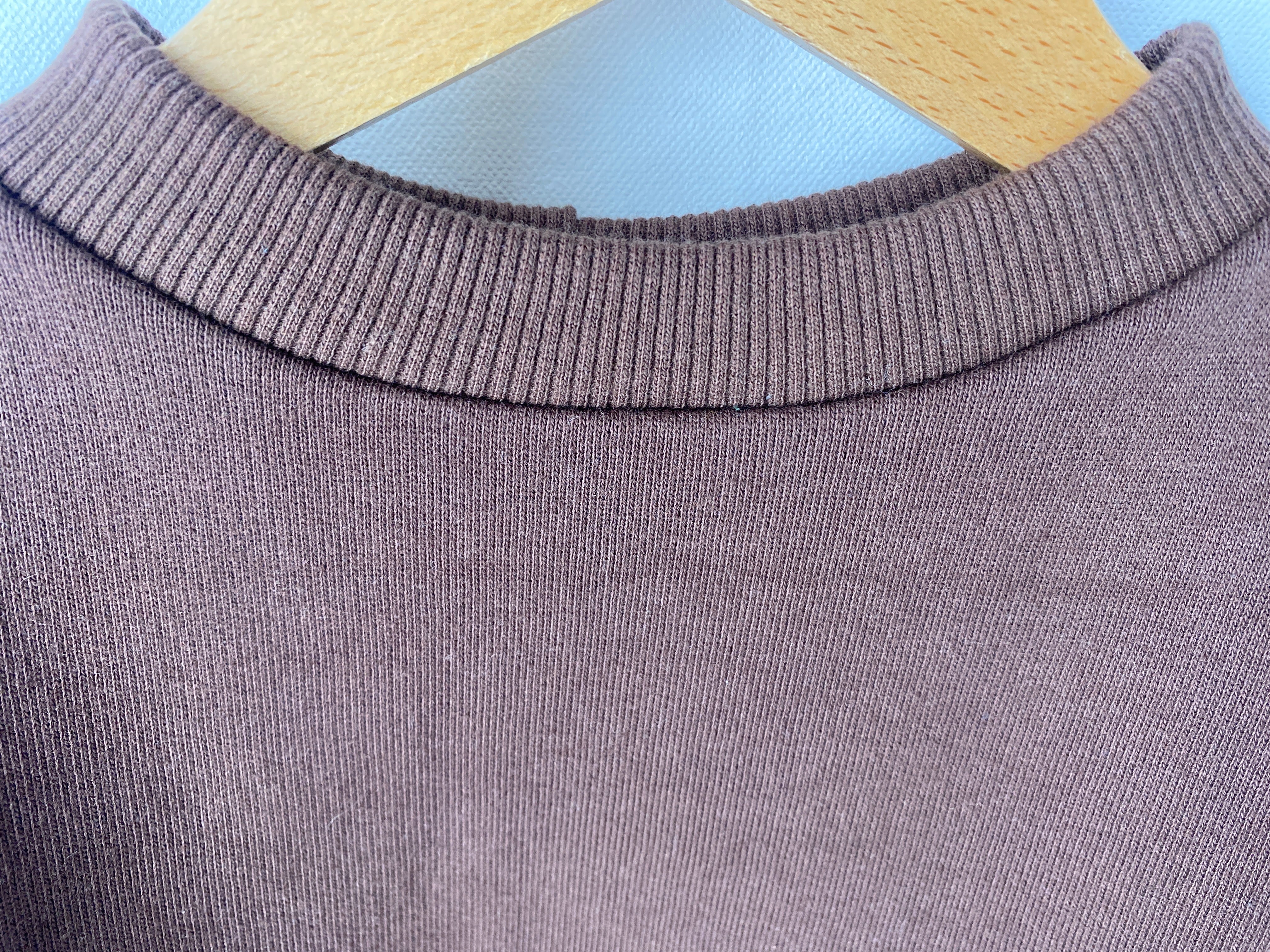 Nahaufnahme des Pulli Bio Sweat Schoko Gr 1Y, zeigt den gerippten Rundhalsausschnitt eines braunen, neuen Strickpullovers. Ein leichter Strich im Stoff ist vorne sichtbar.
