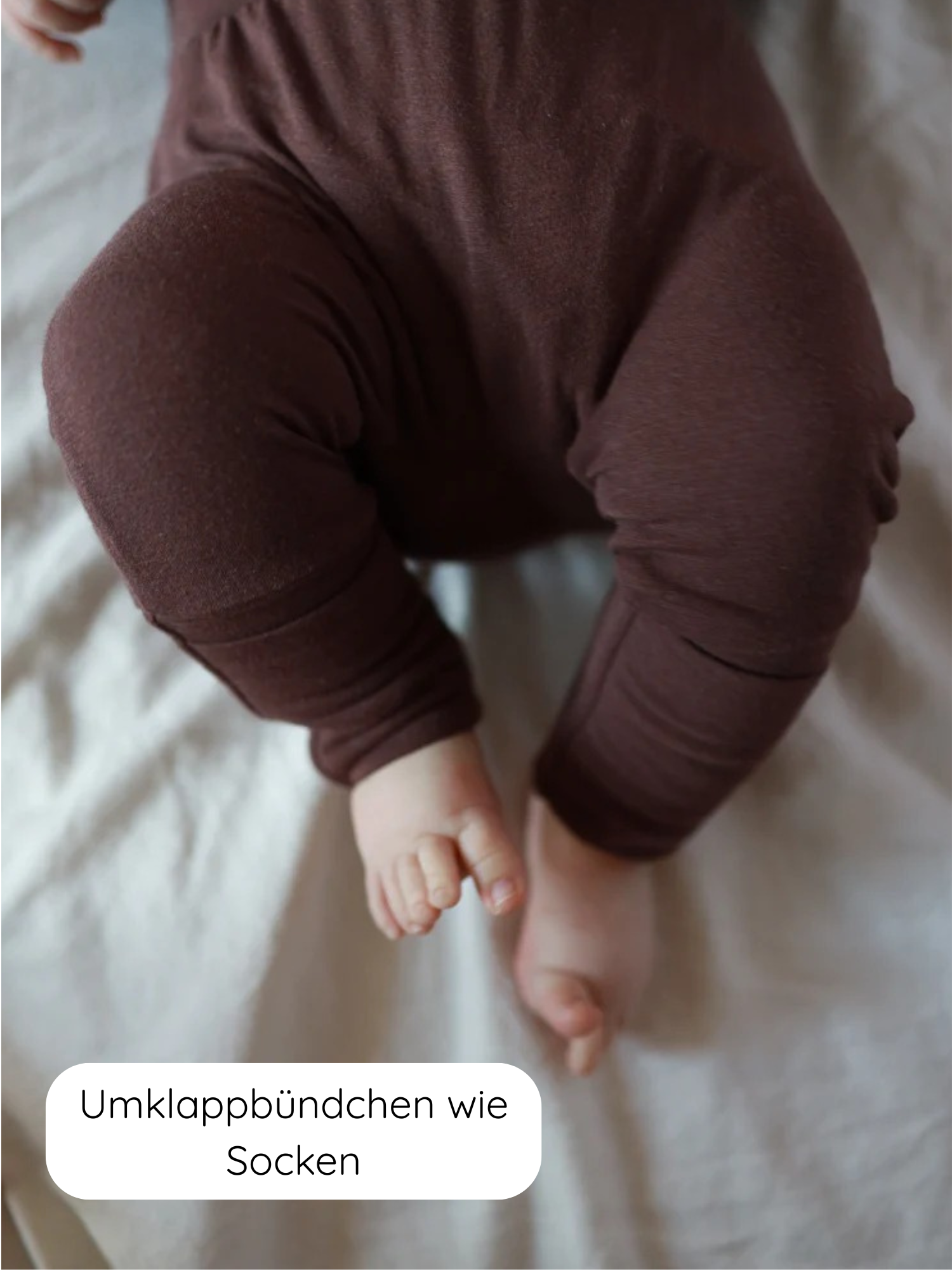 Babyknicker Bambusviskose Zartbitter zeigt die Beine eines Babys in braunem, elastischem Schlafanzug mit umklappbaren Bündchen an den Knöcheln, die wie eingebaute Socken wirken, und winzigen Zehen.