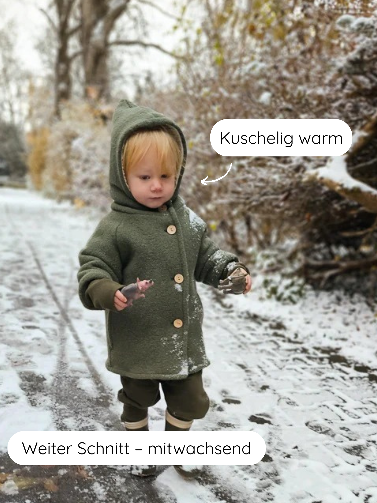 Kleinkind in Teddy-Wichteljacke Wollwalk - Pistazie mit Kapuze und Holzknöpfen, auf einem schneebedeckten Pfad. Hält Spielzeugtier und Zapfen, zeigt robusten, funktional-warmen Wintermantel.