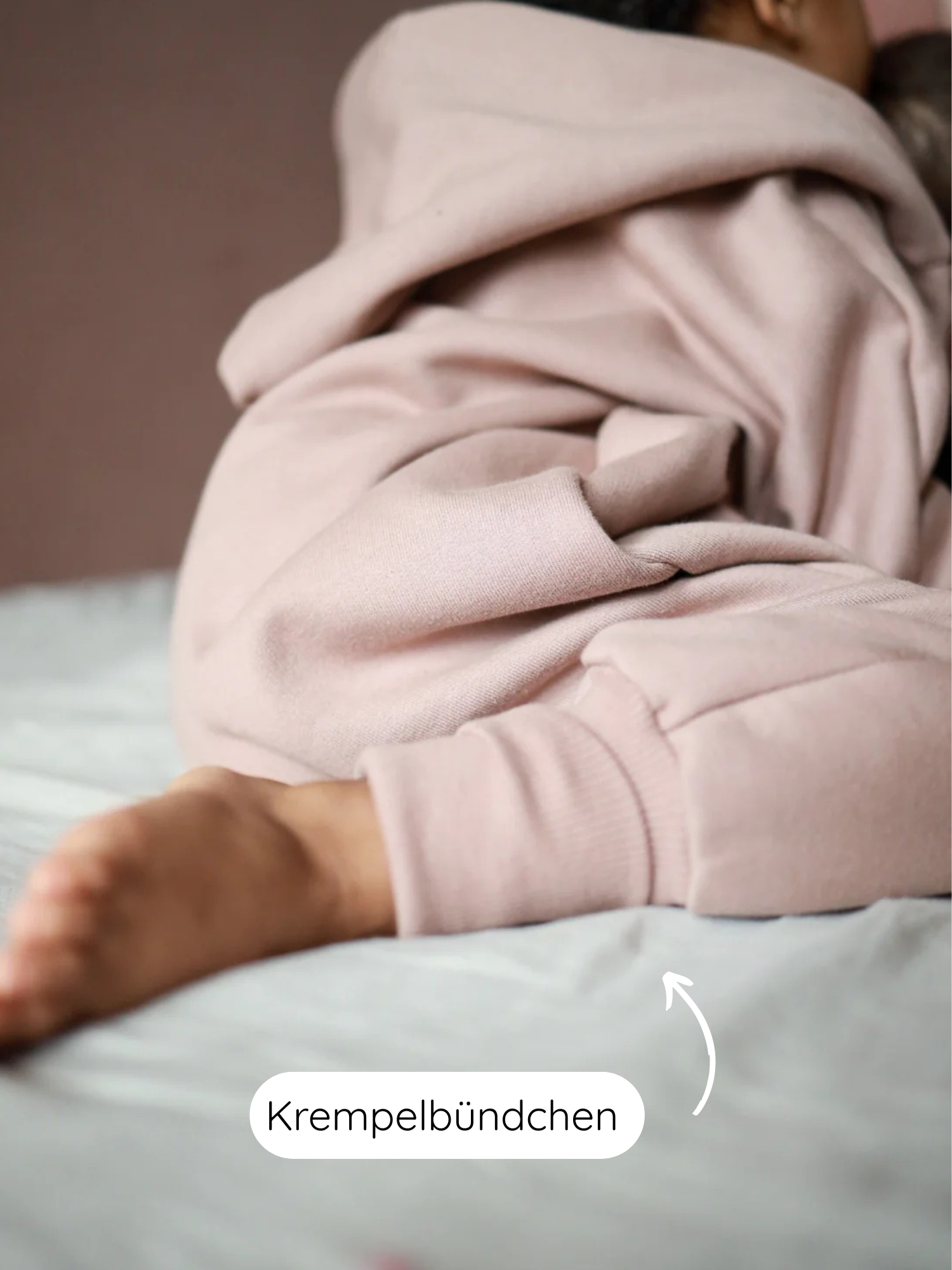 Nahaufnahme eines Kindes im Kuschelanzug Bio-Sweat - Puder mit Wichtelkapuze, zeigt Krempelbündchen am Knöchel für längeres Mitwachsen, aus weicher, angerauter Bio-Baumwolle für gemütlichen Tragekomfort.