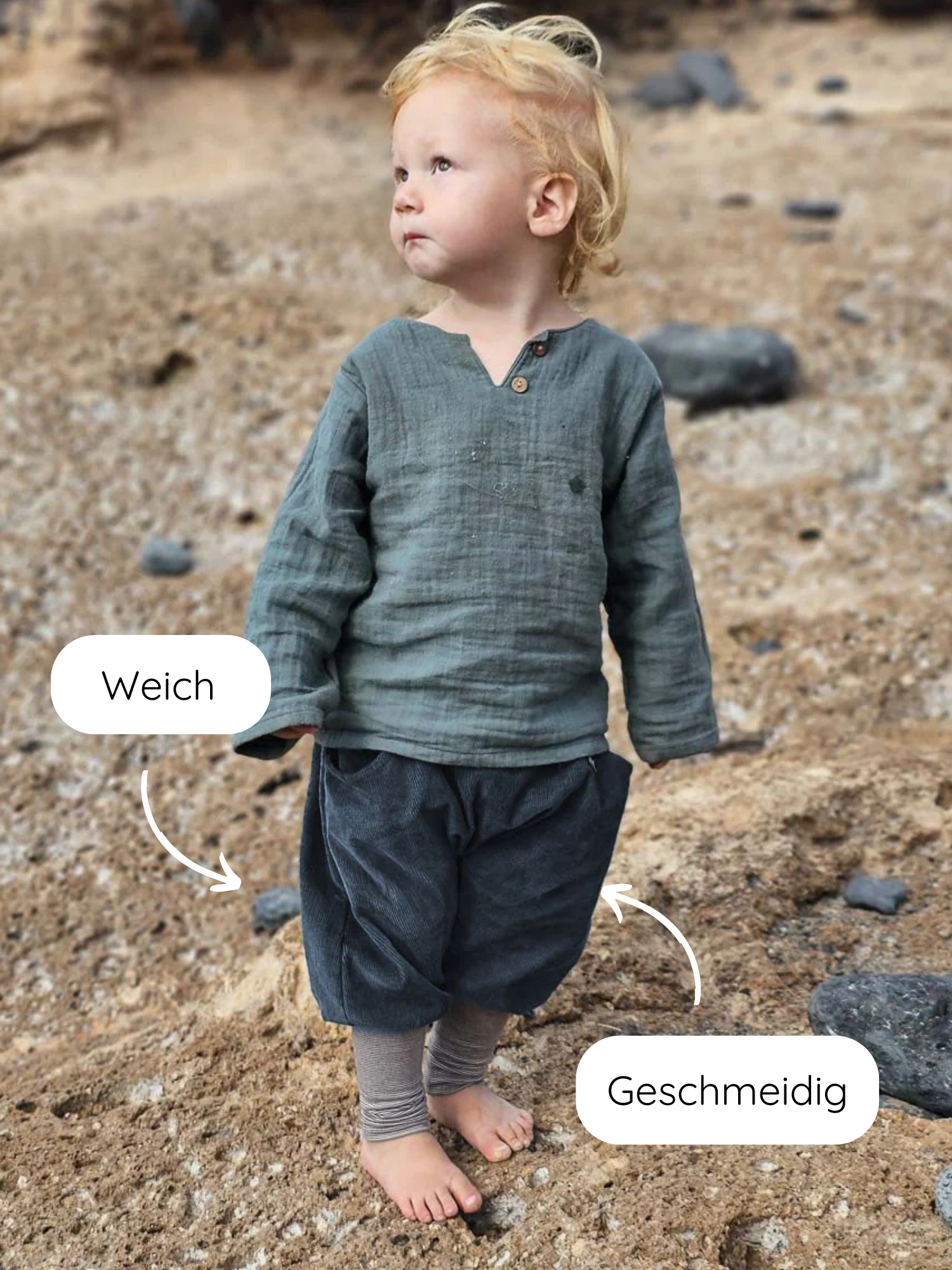 Ein Kleinkind trägt Knickerbocker Feincord Ringel - Blaubeere, gekennzeichnet als weich und geschmeidig, mit einem gestreiften Bund, ideal für Bewegungsfreiheit, auf einem sandigen Strand stehend.