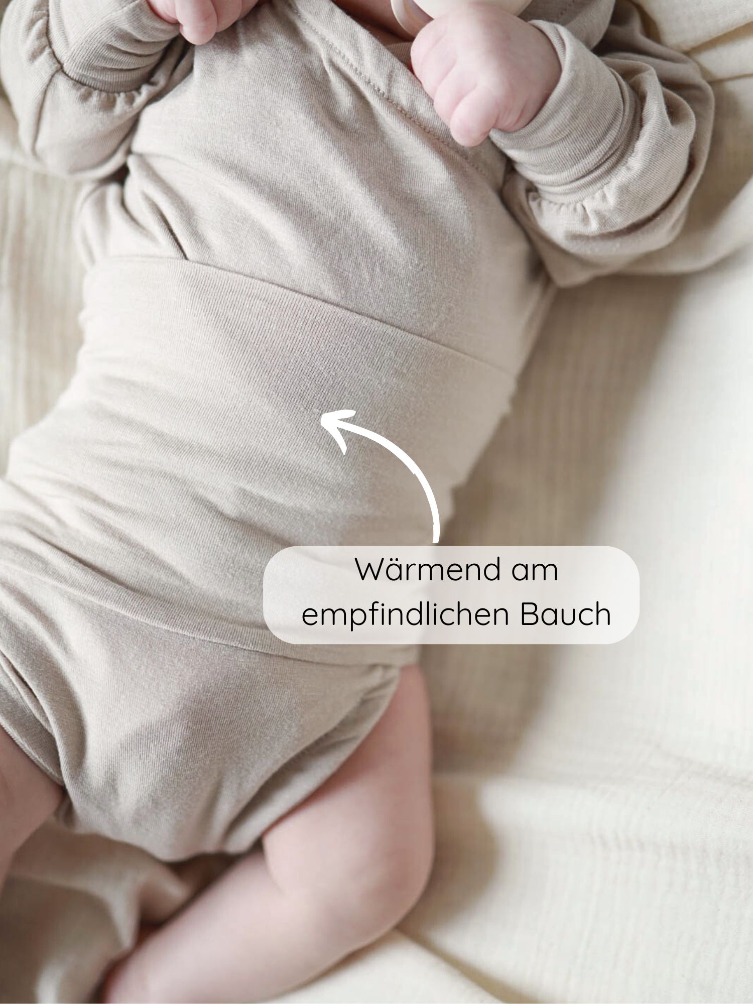 Loopbody Kaschmir-Mix - Sand: Baby trägt weichen, beigen Einteiler. Pfeil zeigt auf den Bauch mit Text Wärmend am empfindlichen Bauch, betont die wärmende Funktion des Kleidungsstücks.