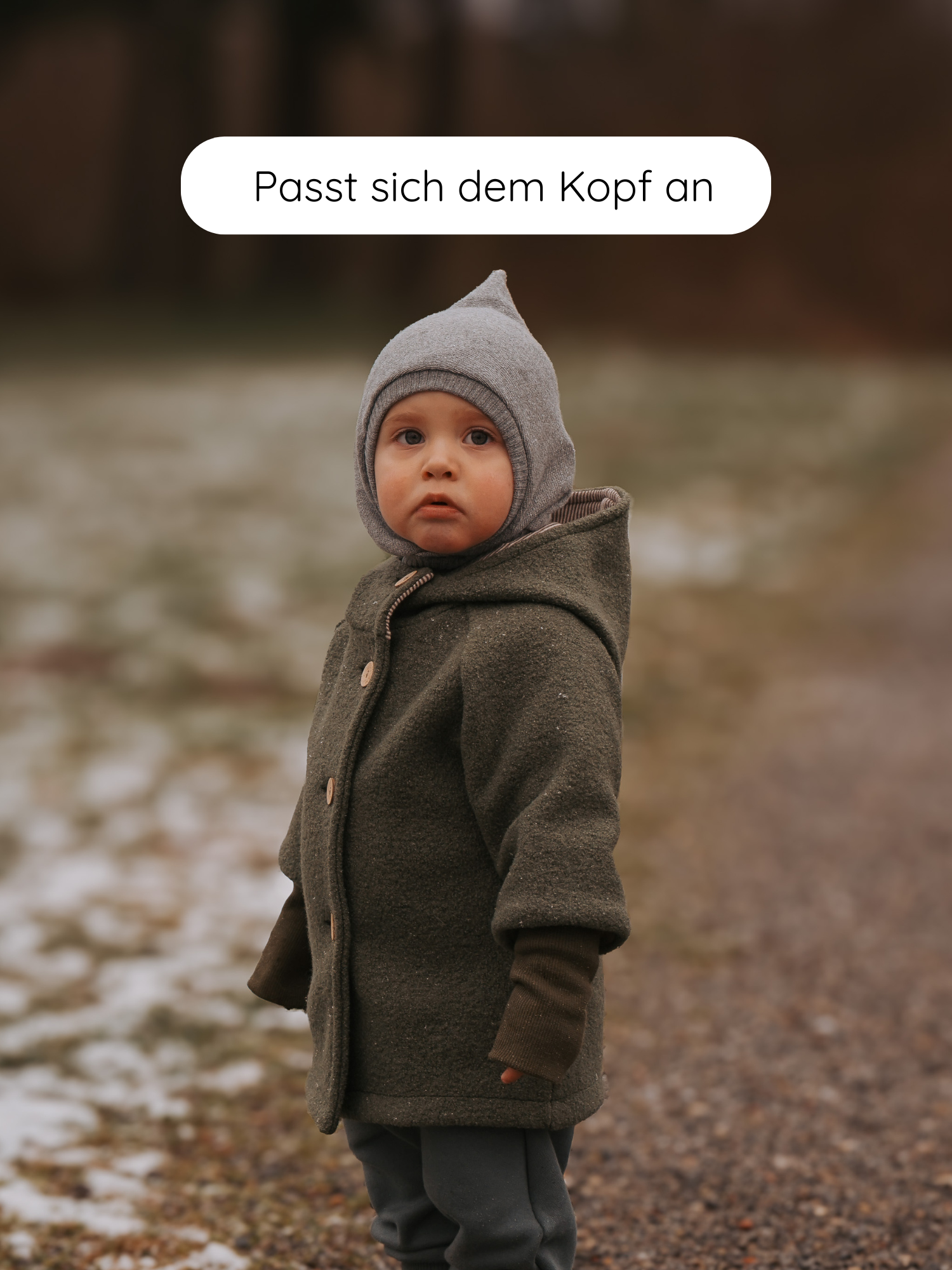 Kleinkind im Freien mit Schlupfmütze Strick - Maus: Graue, spitze Strickmütze mit Ohrenabdeckung. Text Passt sich dem Kopf an schwebt darüber, betont die anpassbare Passform der Mütze.