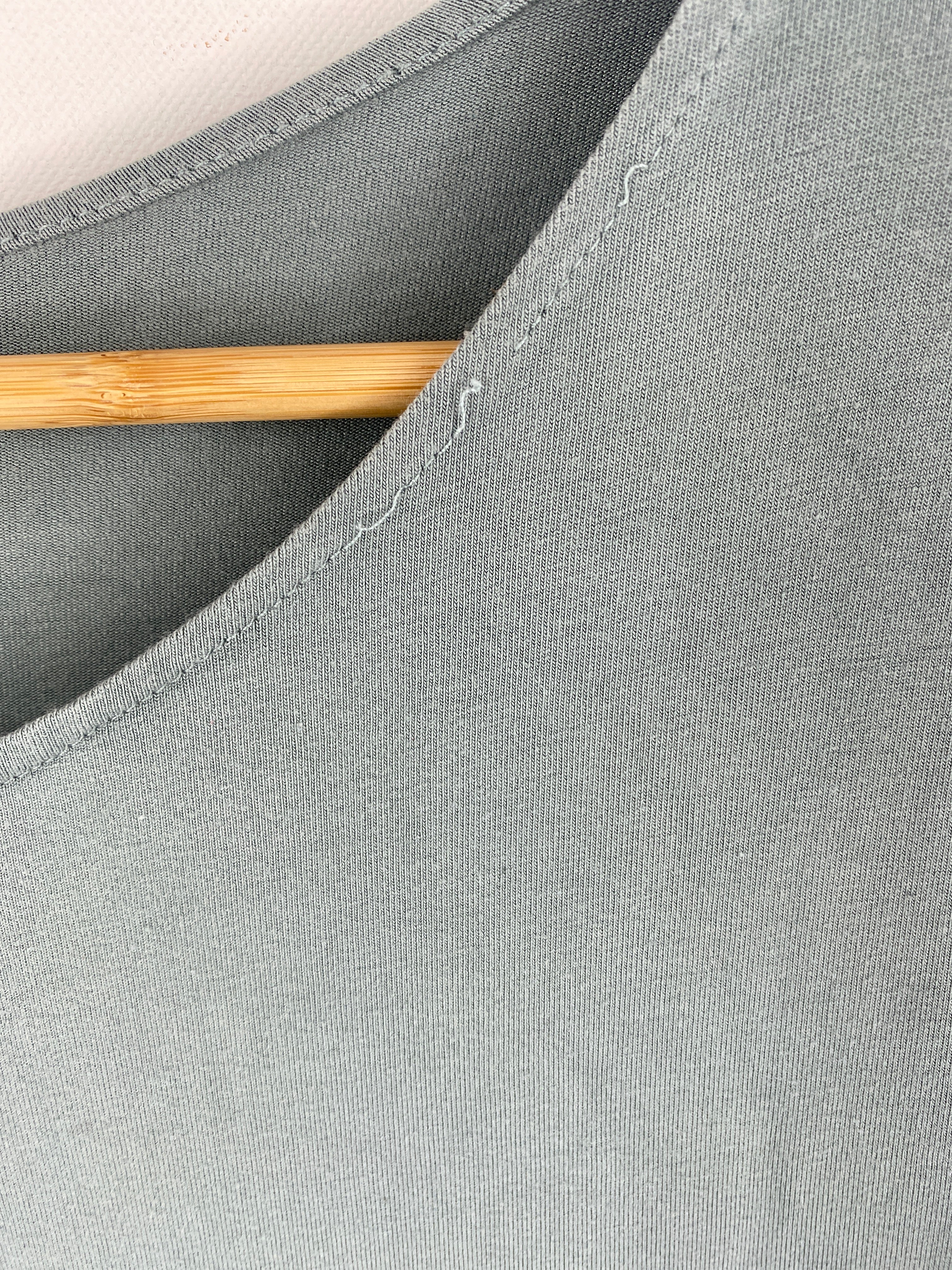 Nahaufnahme eines „Kopie“ Kleids aus Bio-Jersey in hellblau, Größe S, auf einem glatten Holzkleiderbügel. Eine Naht am Halsausschnitt ist locker, mit kleinem Fleck vorne sichtbar.