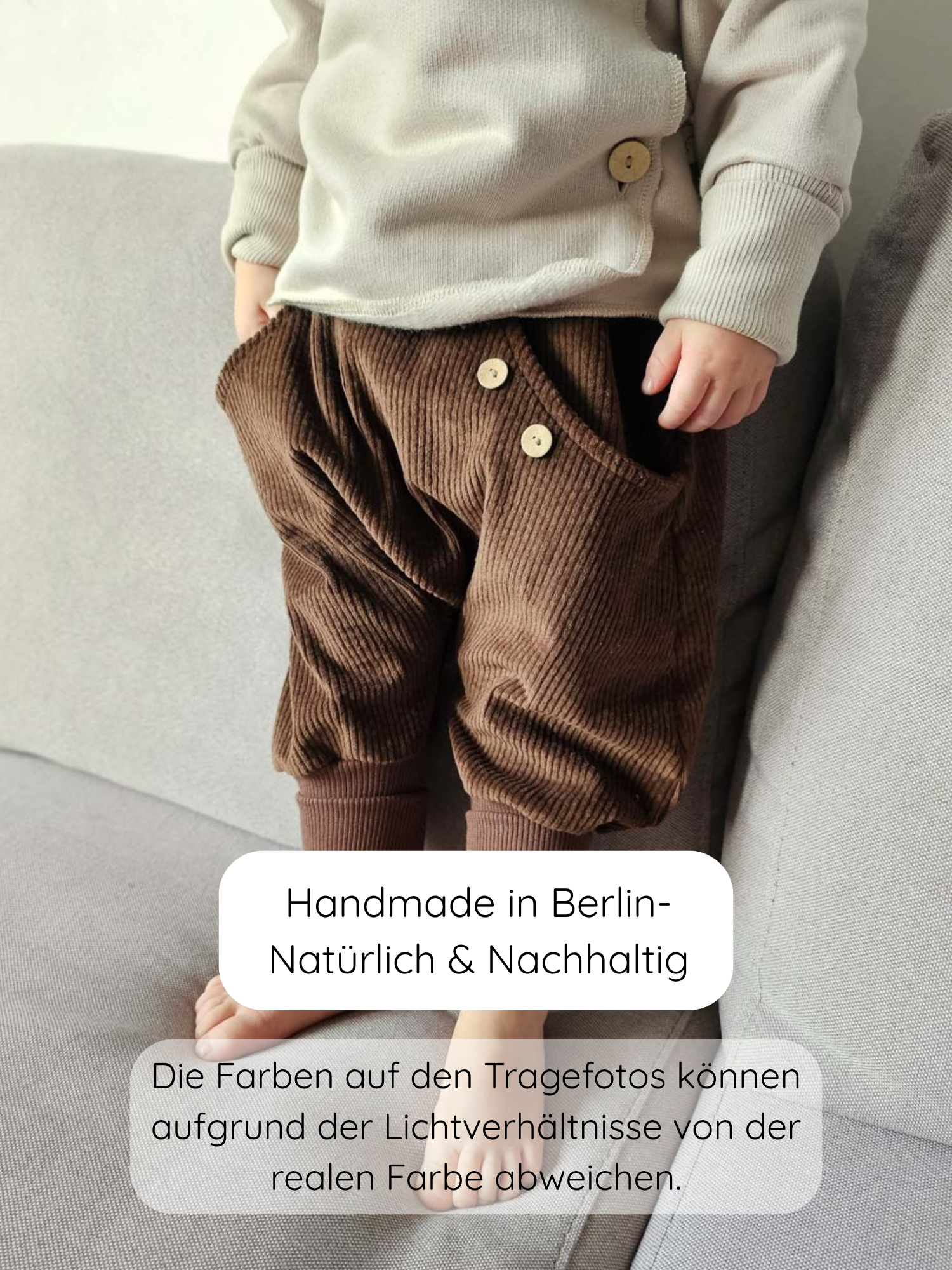Kleinkind steht barfuß auf einem Sofa, trägt Knickerbocker Breitcord - Schoko: braune Cordhose mit Holzknöpfen, kombiniert mit cremefarbenem Langarmshirt. Hochwertige, handgefertigte Kinderbekleidung aus Berlin.