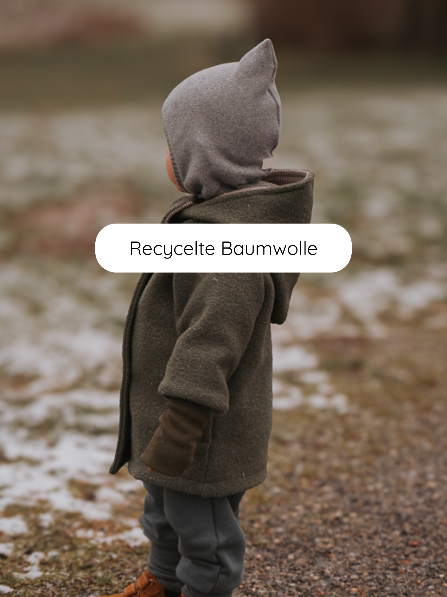 Kleinkind auf verschneitem Weg trägt die Schlupfmütze Strick - Maus, eine graue Strickmütze mit spitzen Ohren, die Kopf und Hals warm hält. Perfekt für kalte Tage.