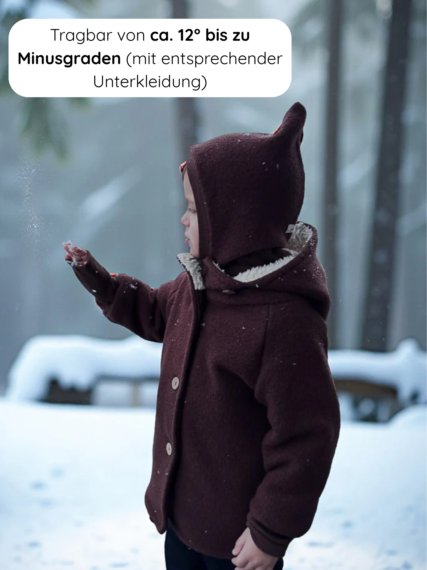 Kleinkind im Schnee trägt die Winter Wichteljacke Wollwalk - Schoko, mit Knöpfen und Kapuze mit Ohren, ideal für kalte Temperaturen. Mit Teddyfutter für Wärme und Komfort.