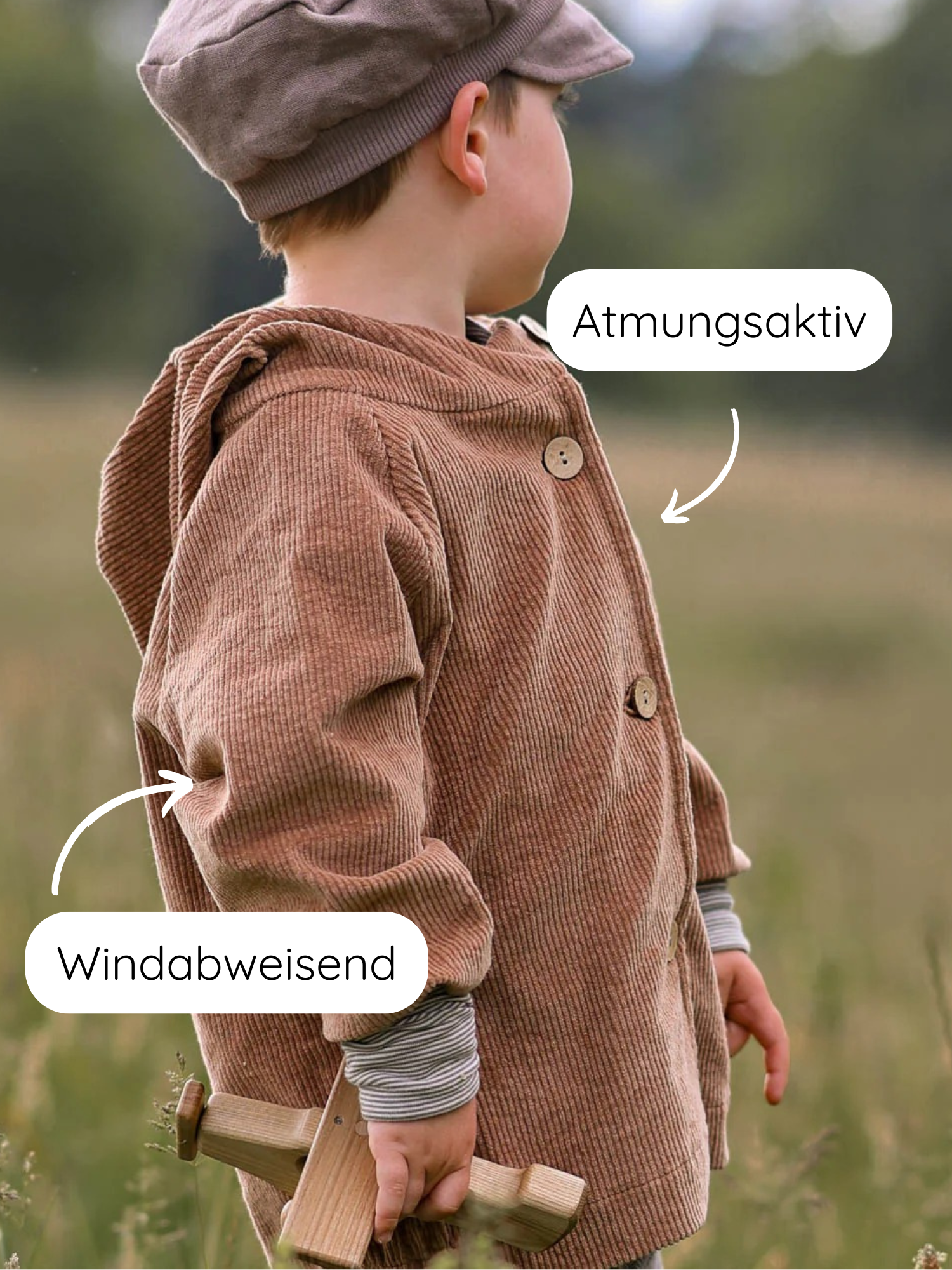 Ein Kind hält ein Holzflugzeug und trägt die Wichteljacke Breitcord Stretch - Weizen mit Wichtelkapuze. Sie ist atmungsaktiv und windabweisend, mit krempelbaren Armbündchen für mitwachsendem Komfort.