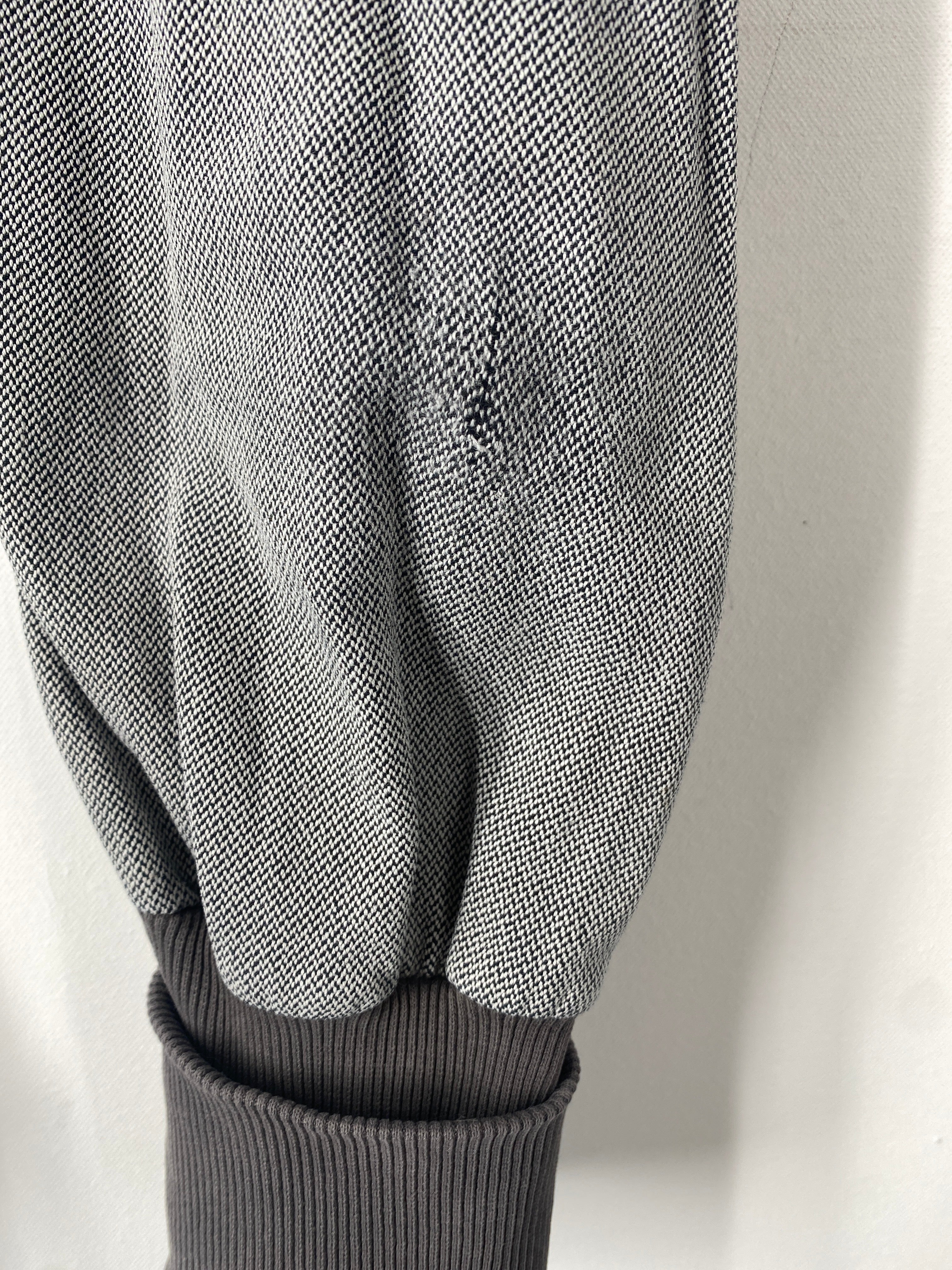 Knickerbocker Bio Kreuzköper Maus Gr 4/5Y: Nahaufnahme eines grauen Ärmels mit fein gewebtem Stoff, leicht beschädigt über dem dunklen, gerippten Bündchen. Zustand: gut, mit kleinem Stofffehler.