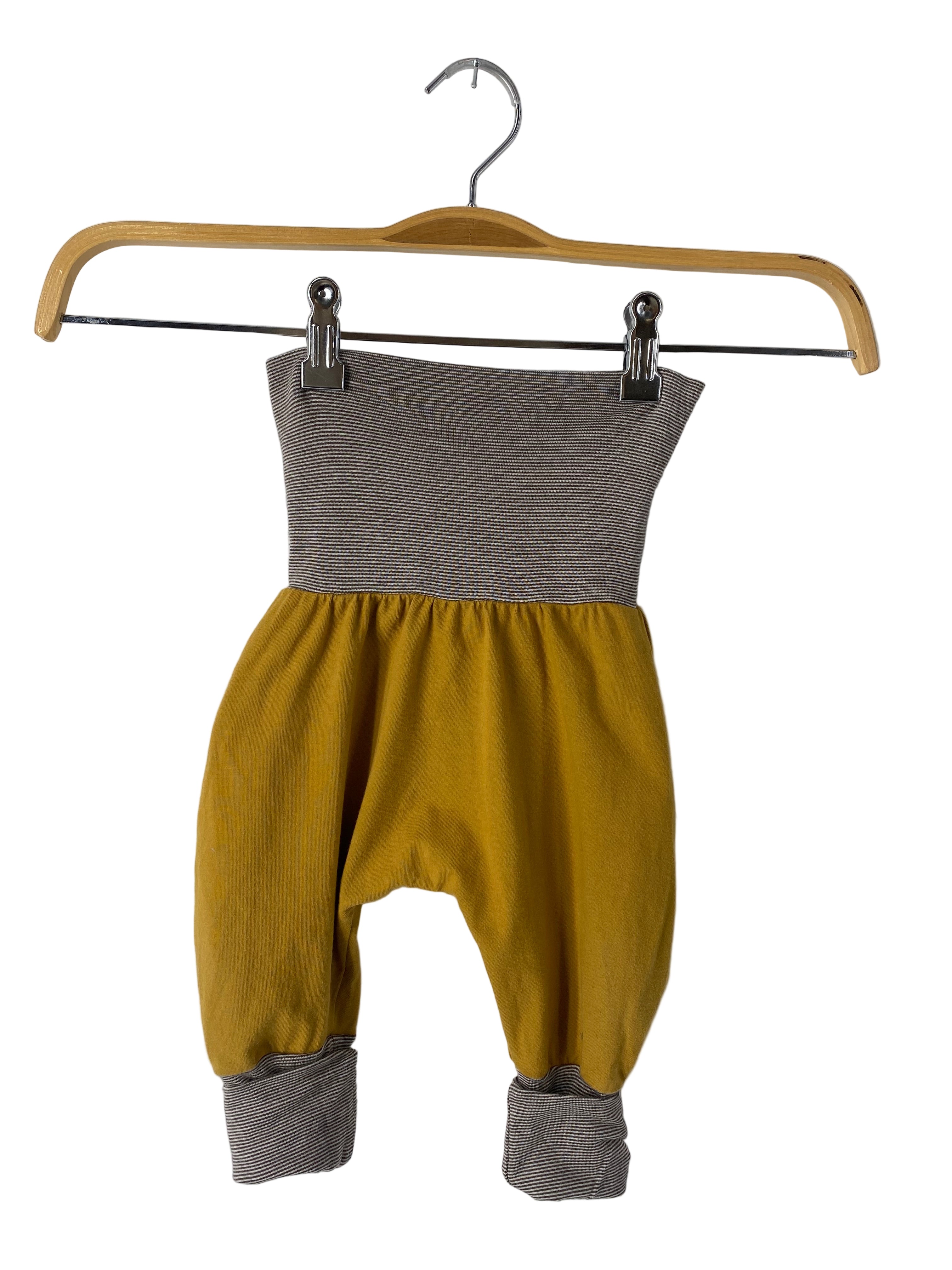 Babyknicker Jersey Kurkuma Gr 3M: Mustardfarbene Haremshose mit breitem, umschlagbarem grau-weiß gestreiftem Bund und passenden Bündchen, hängt an einem Holzkleiderbügel. Zustand: sehr gut.