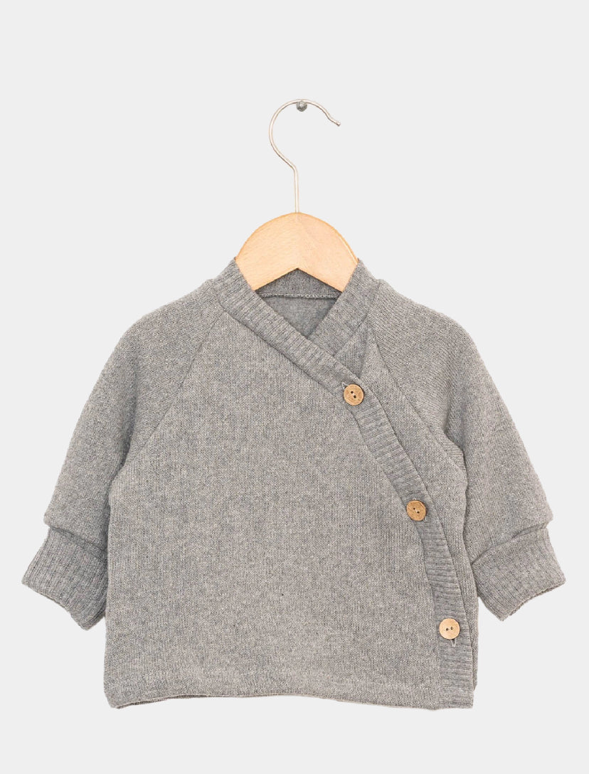 Kleiner, hellgrauer Strickcardigan für Babys, im Wickelstil mit drei diagonalen Holzköpfen. Produktname: (Kopie) Schlüttli Strick Maus Gr 1Y. Zustand: neu. Hängt an einem schlichten Holzbügel.
