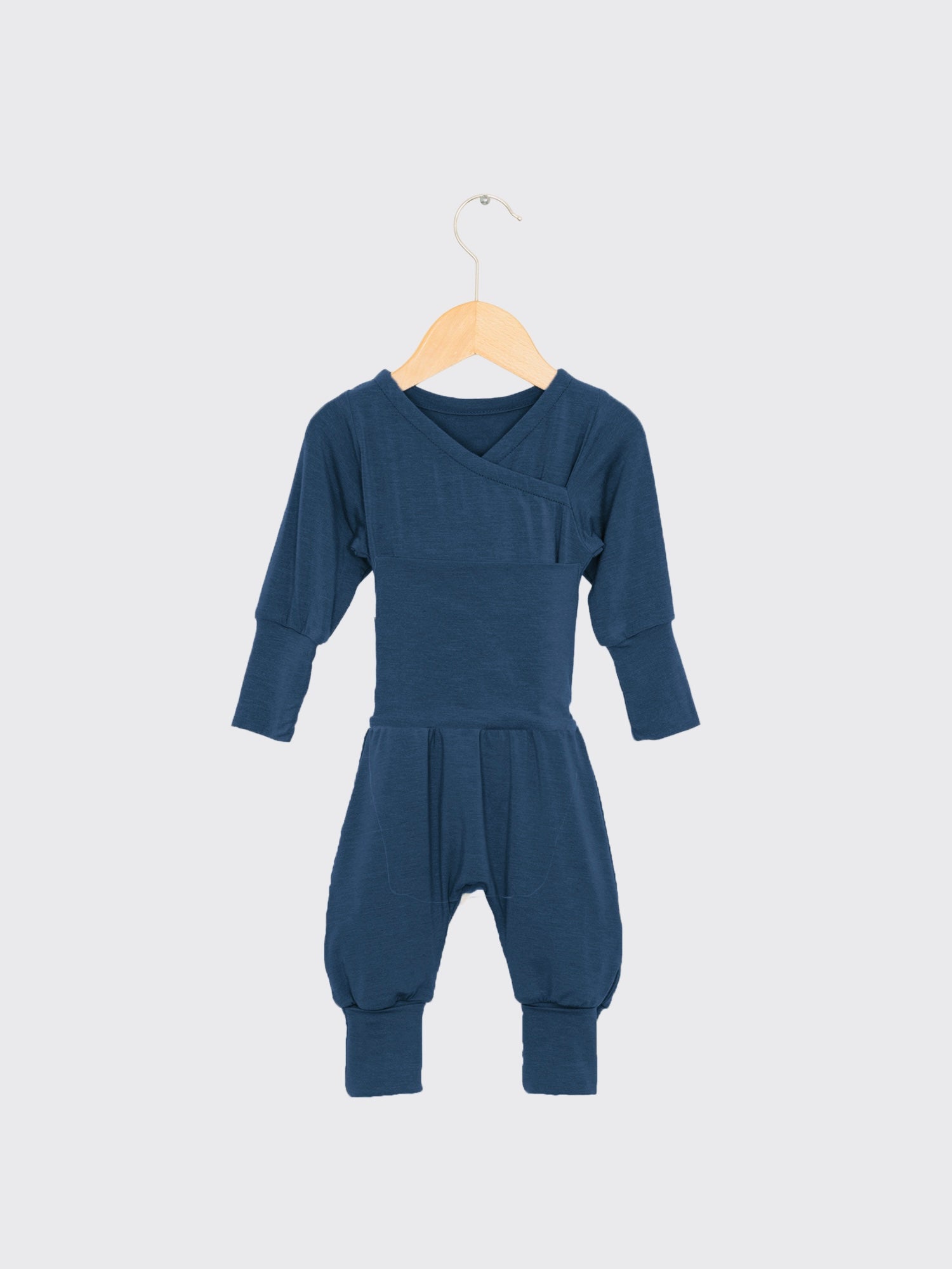 Loopstrampler Kaschmir-Mix - Blaubeere: Ein navyblauer, langärmliger Babystrampler ohne Knöpfe, mit kimonoartigem Ausschnitt und umklappbaren Bündchen an den Beinen, auf einem Holzbügel hängend.