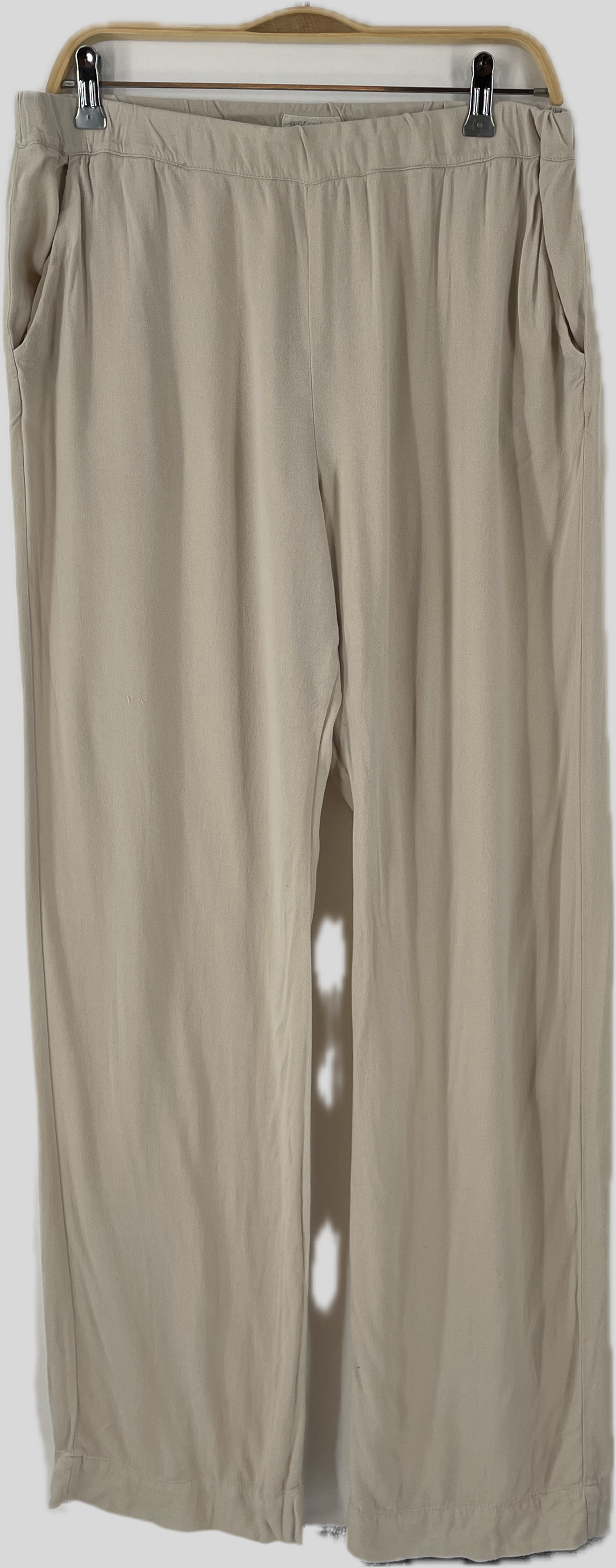 Frauen Hose Crepe Sand Gr. M/L: Leicht-beige, weite Lounge-Hose mit elastischem Bund und Seitentaschen, aus weichem, fließendem Stoff, auf einem Holzkleiderbügel hängend. Ideal für komfortable, stilvolle Tage.