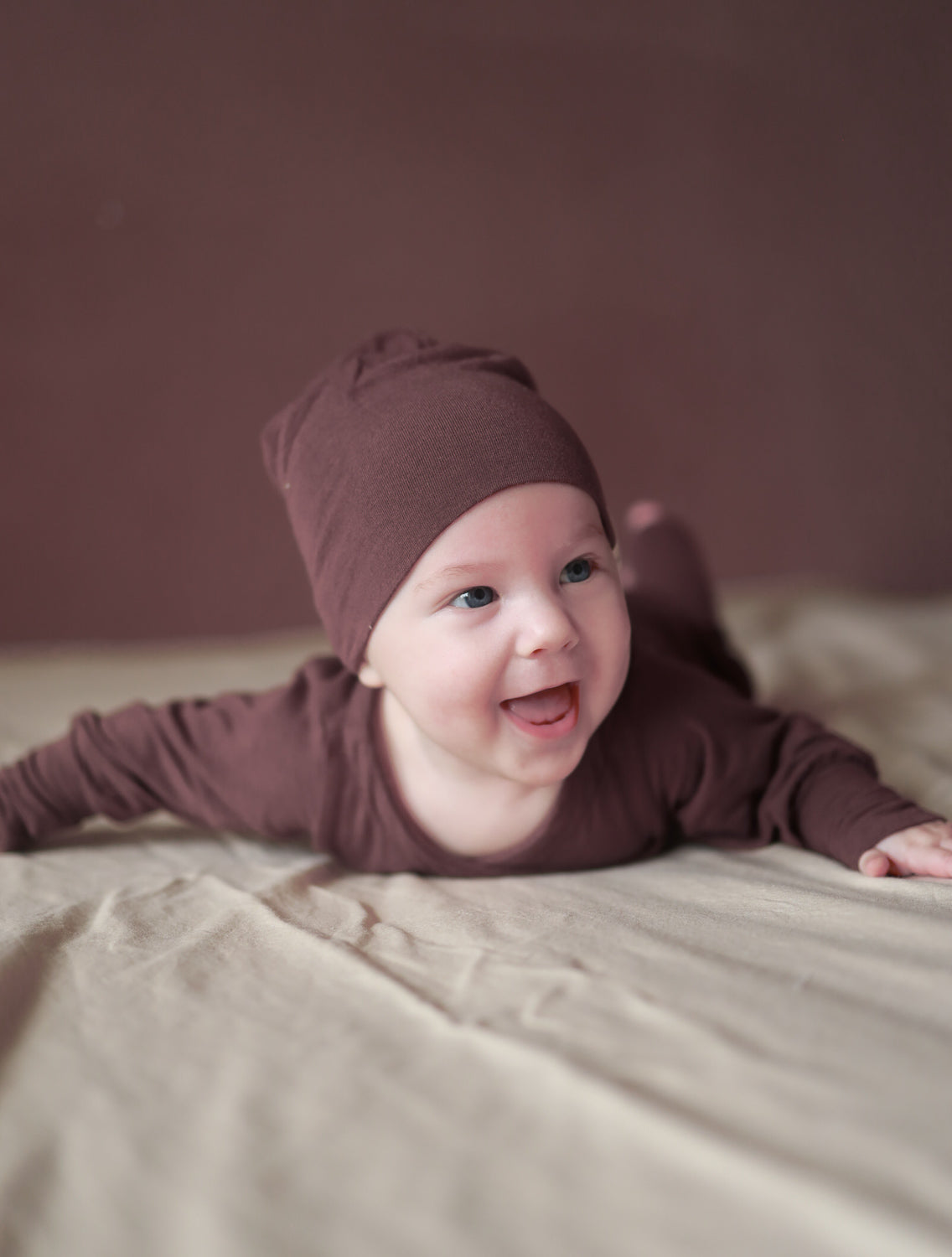 Ein Baby liegt auf dem Bauch und trägt die Beanie Kaschmir-Mix - Malve, eine handgefertigte, weiche Beanie-Mütze aus Kaschmir-Micromodal-Mix, ideal für kühle Jahreszeiten. Baby Body und Erstausstattung Baby