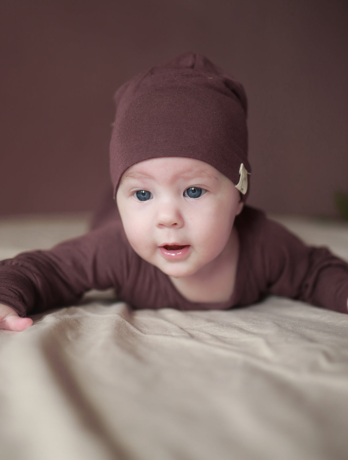 Baby, das auf dem Bauch liegt, trägt die Beanie Kaschmir-Mix - Malve, eine weiche, leichte Mütze, die den Kopf schützt. Perfekt für kühle Jahreszeiten und unter Helmen tragbar. Baby Body und Erstausstattung Baby