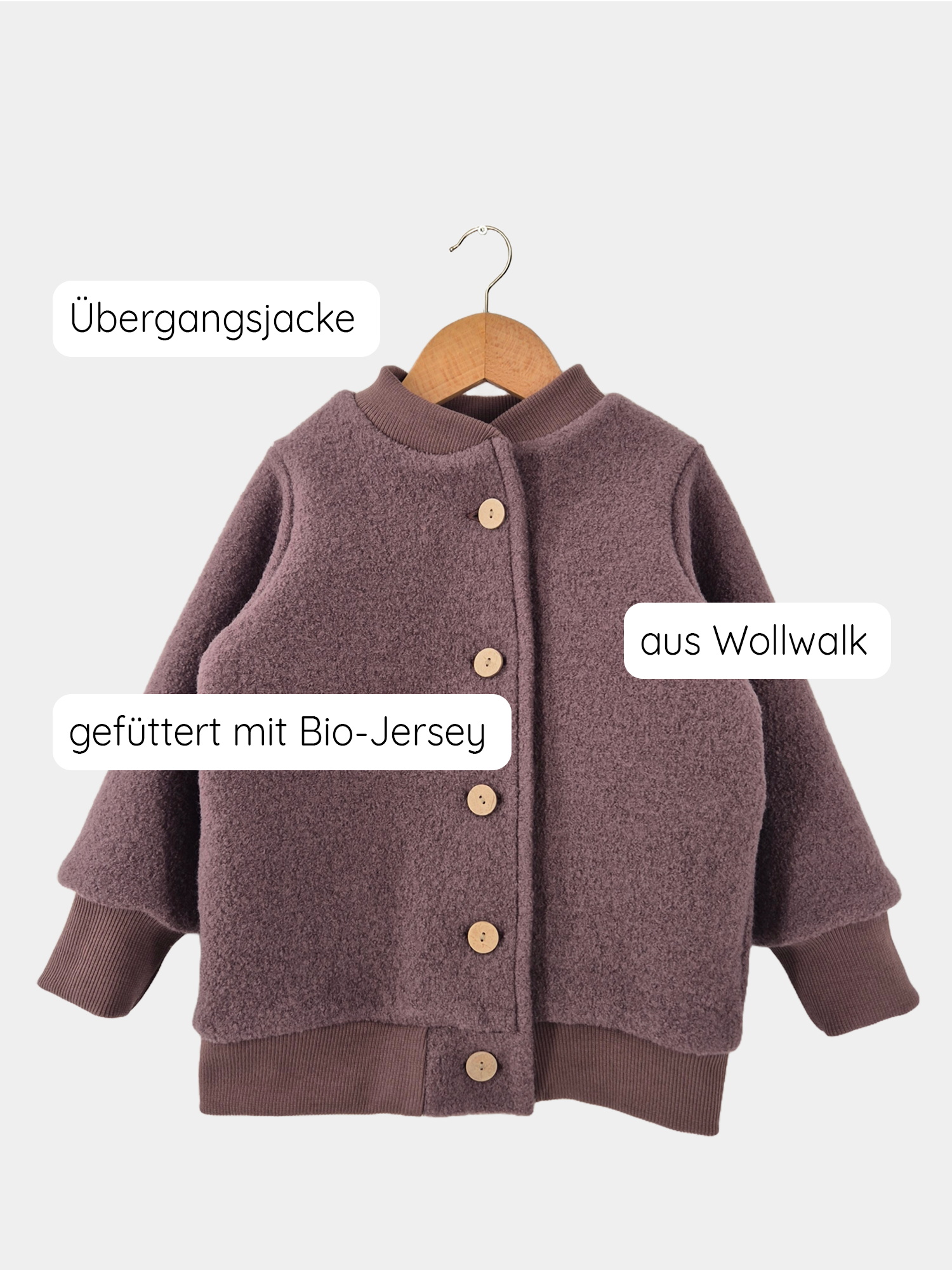 Bomberjacke Wollwalk - Malve auf einem Holzkleiderbügel, mit Knöpfen und weichem Jerseyfutter, gezeigt auf einer Schaukel. Nachhaltig in Berlin produziert, bietet sie Wärme und Langlebigkeit für Kinder.