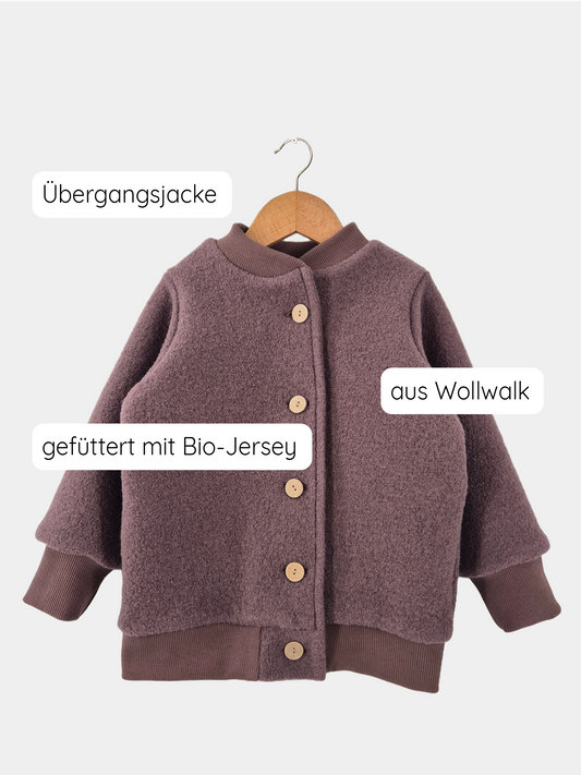 Giacca bomber in lana cotta color malva su una gruccia di legno, con bottoni e morbida fodera in jersey, mostrata su un’altalena. Prodotta in modo sostenibile a Berlino, offre calore e durata ai bambini.
