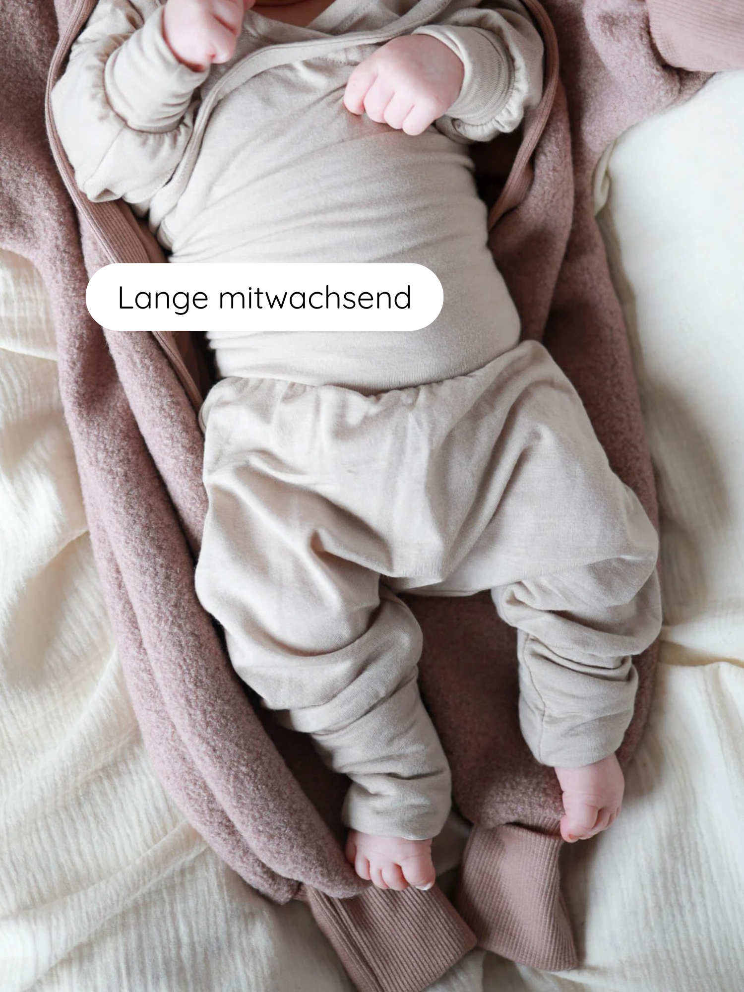 Ein Kleinkind trägt einen Babyknicker Kaschmir-Mix - Sand, bestehend aus weichem, neutral-beigem Langarmbody und mitwachsenden Hosen mit Klappbündchen, auf einer flauschigen Decke liegend.