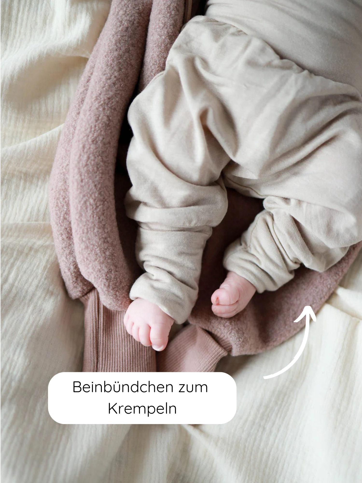 Babyknicker Kaschmir-Mix - Sand mit umklappbaren Beinbündchen, die die kleinen Füße wärmen. Die Hose liegt auf einer hellbraunen Decke, ein weißer Pfeil zeigt auf das krempelbare Bündchen.