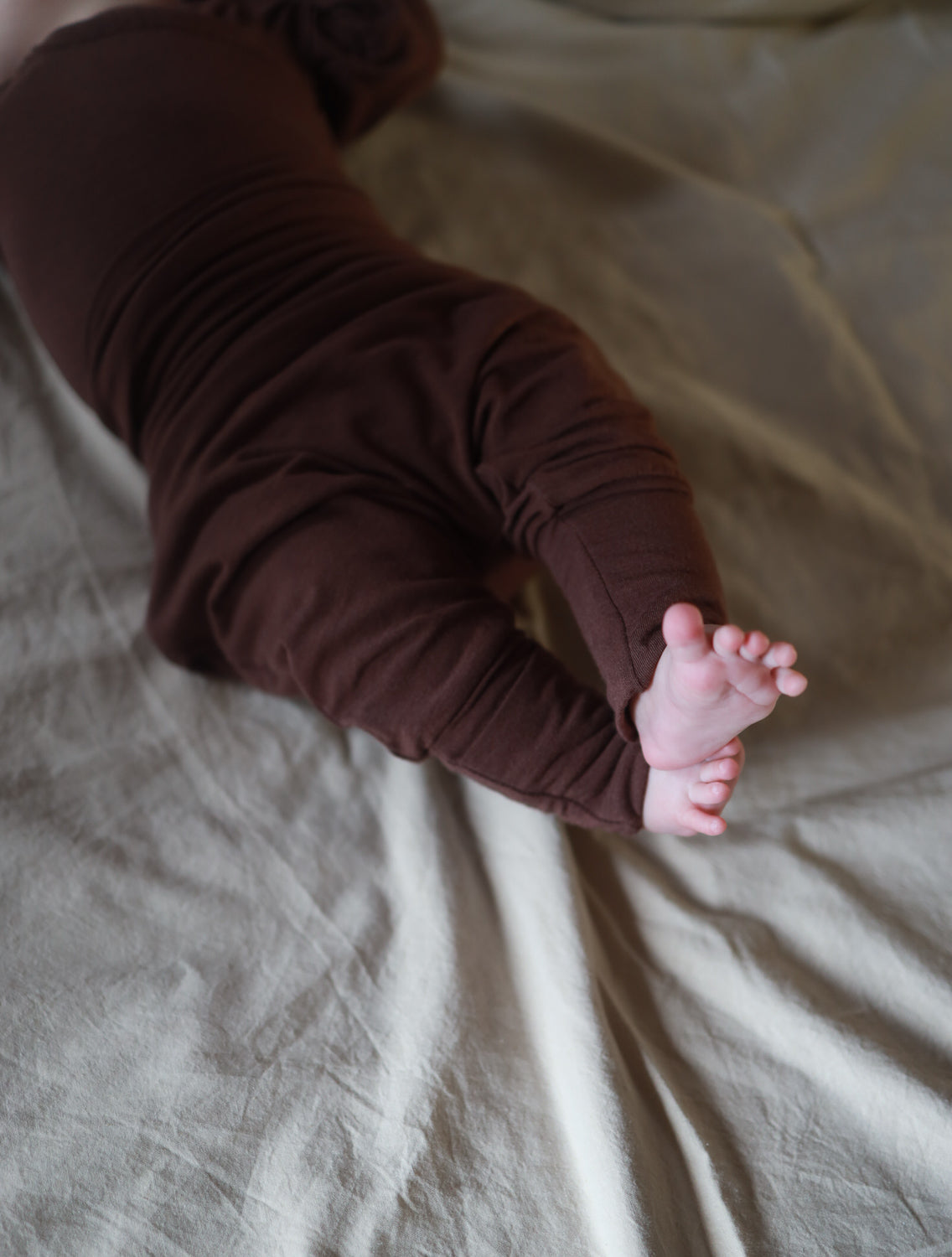 Babyknicker Kaschmir-Mix - Malve: Ein Baby liegt auf einem Bett, trägt weiche Babyhose mit Klappbündchen, ideal für Wärme und Komfort. Perfekt kombiniert mit Kaschmir-Mix Loopbody für gemütliche Erstausstattung Baby.