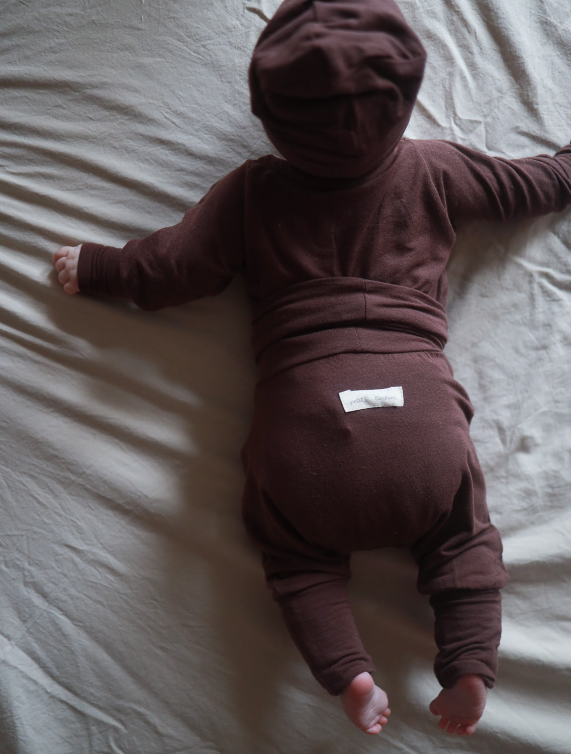 Ein Baby liegt auf dem Bett und trägt die Babyknicker Kaschmir-Mix - Malve mit Klappbündchen, die für Wärme und Komfort sorgt. Sichtbar sind weiche, umklappbare Bündchen an den Beinen. Erstausstattung Baby und Geschenk für Babys.