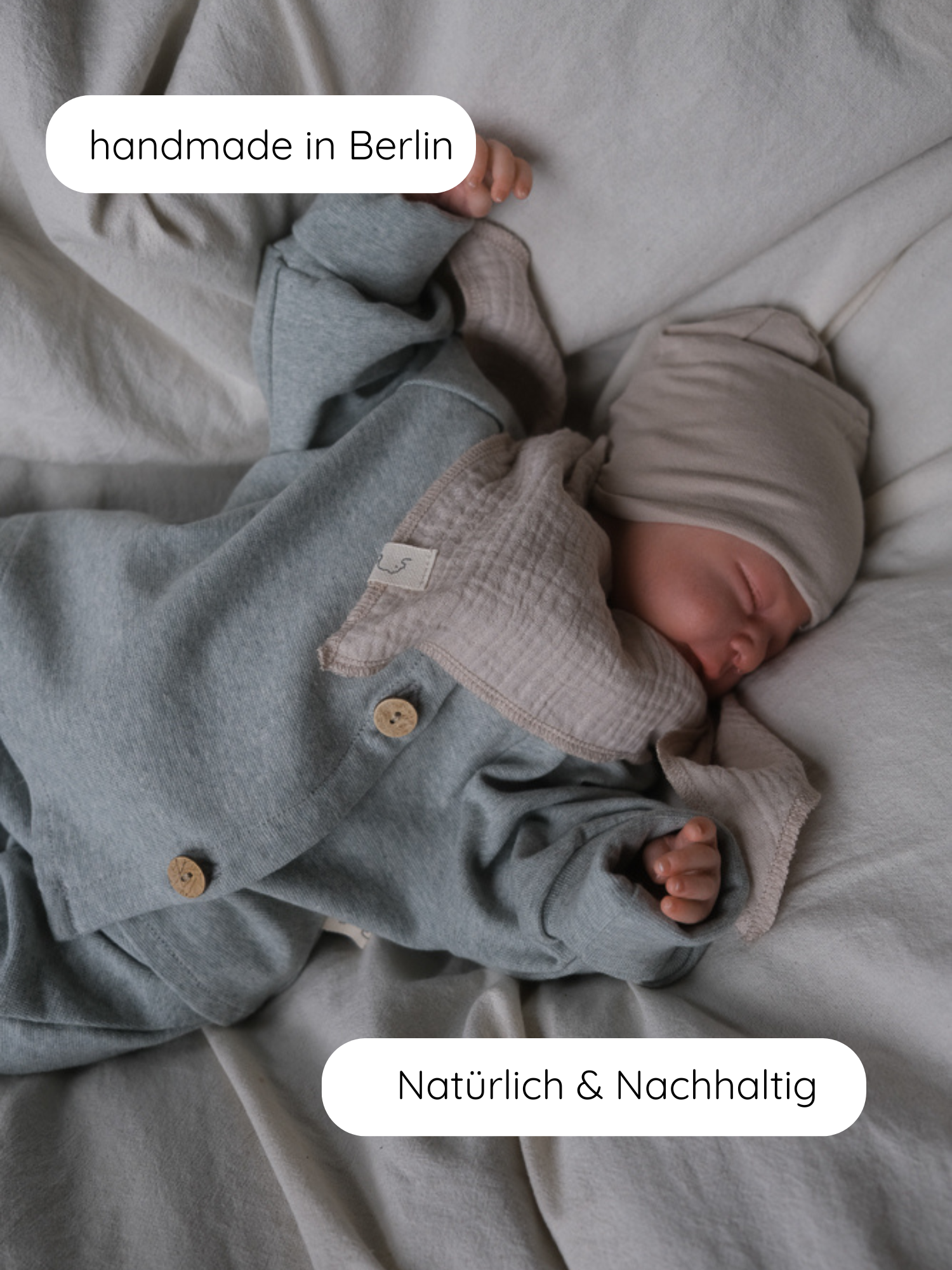 Neugeborenes in neutralem Bettzeug trägt Babyschlüttli Feinstrick - Mint Meliert mit Holzknöpfen, passender Mütze und Muslin-Bib. Labels: handmade in Berlin, Natürlich & Nachhaltig.
