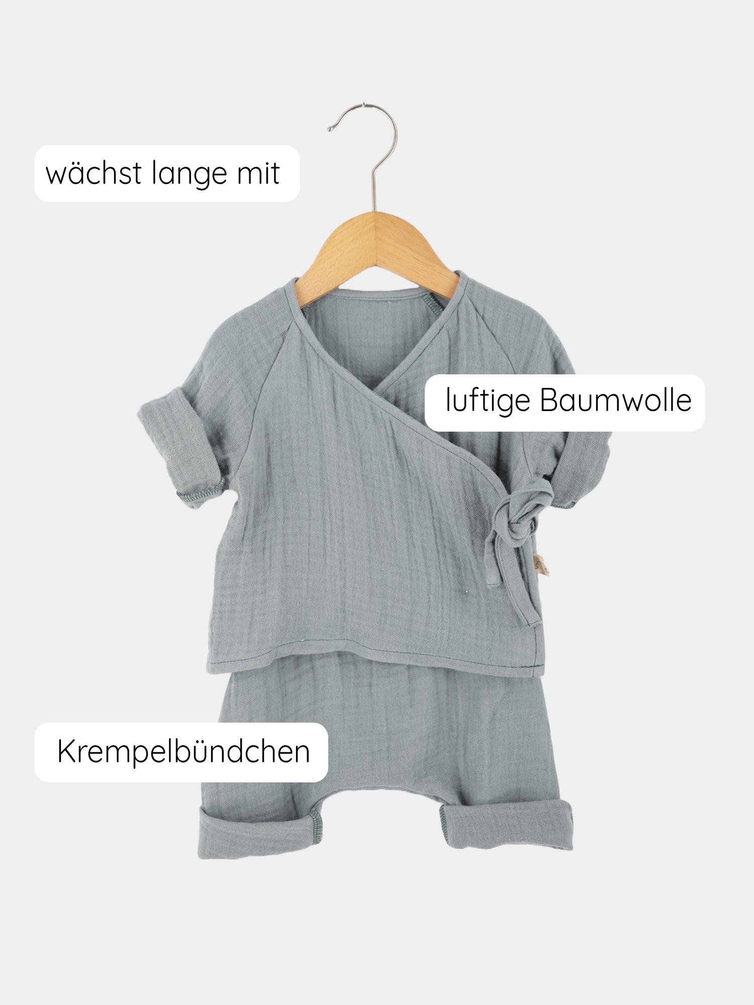 Babyset Baumwoll-Musselin - Eisblau, bestehend aus einem Wickel-Schlüttli und einer Babyhose auf einem Kleiderbügel, zeigt ein luftiges Design mit weiten Ärmeln und Hosenbeinen, ideal für Babys.
