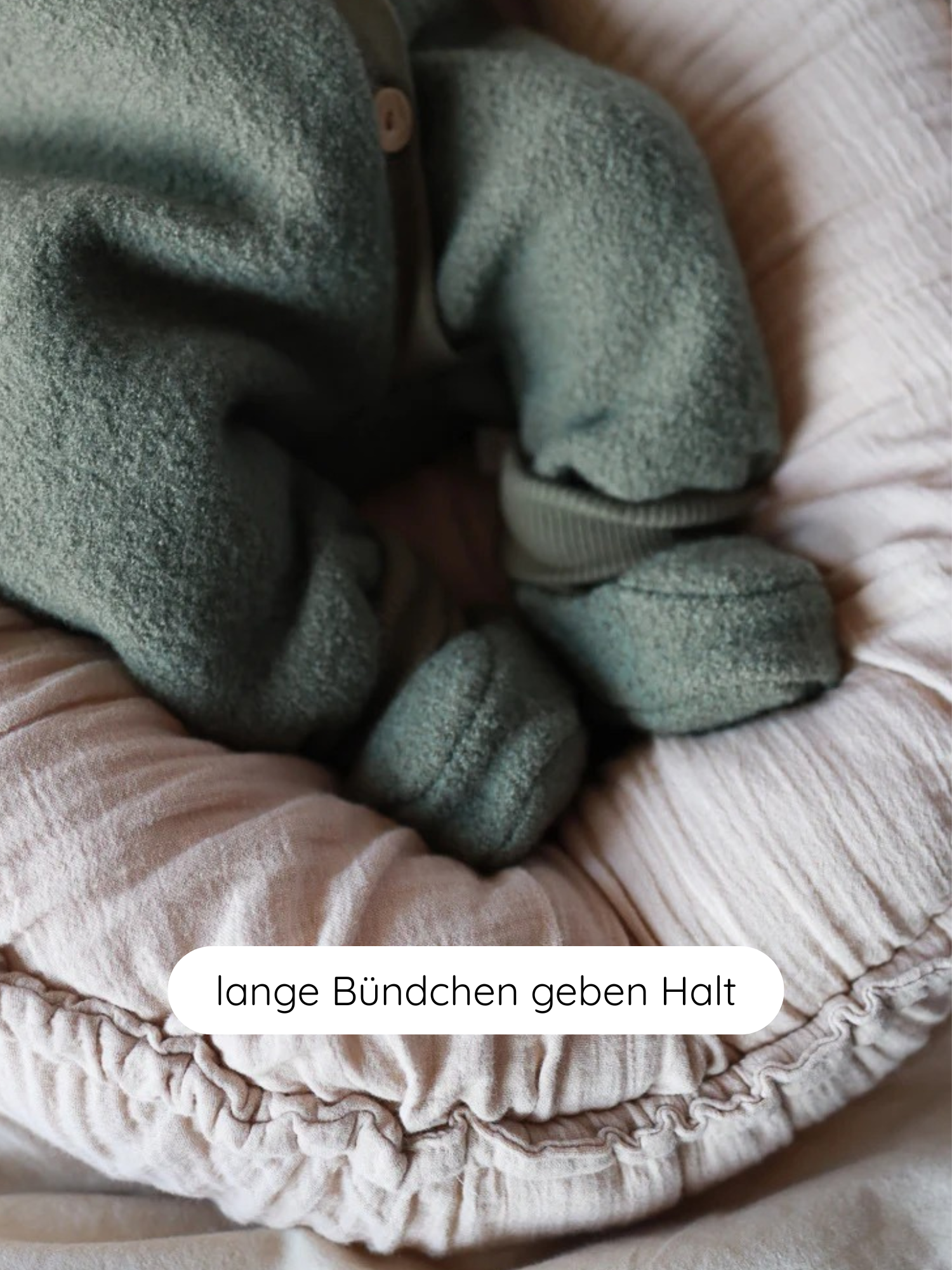 Babybooties Wollwalk - Pistazie: Ein Baby trägt grüne Wollwalk-Booties mit langen Bündchen für Halt, liegend in einem weichen, rosa Baby-Nest. Ideal für die kühle Saison, bieten Wärme und Atmungsaktivität.