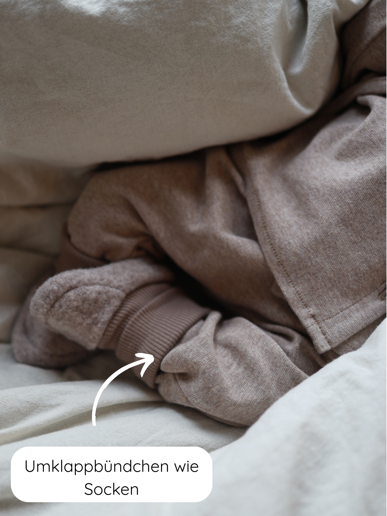 Babyknicker Feinstrick - Hafer Meliert, weicher melierter Feinstrick-Jersey, zeigt umklappbare Bündchen an den Knöcheln wie Socken auf cremefarbener Bettwäsche, ideal zum Krabbeln und Spielen.