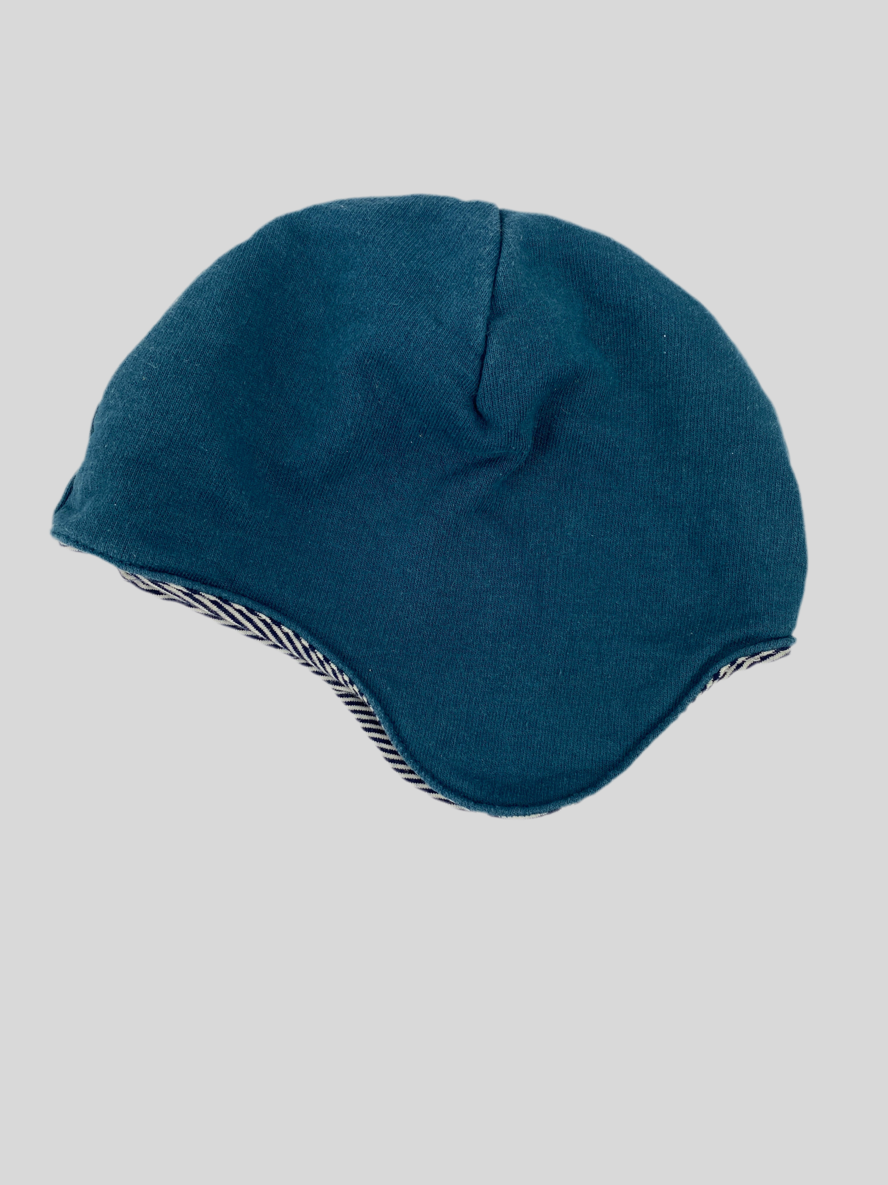 Kopie Baby Mütze blau - Sweat mit Ringel gefüttert Gr 6M zeigt eine beanie‐style Mütze mit sanft geschwungenen Ohrenklappen und sichtbarem gestreiftem Futter am unteren Rand. Zustand: gut.