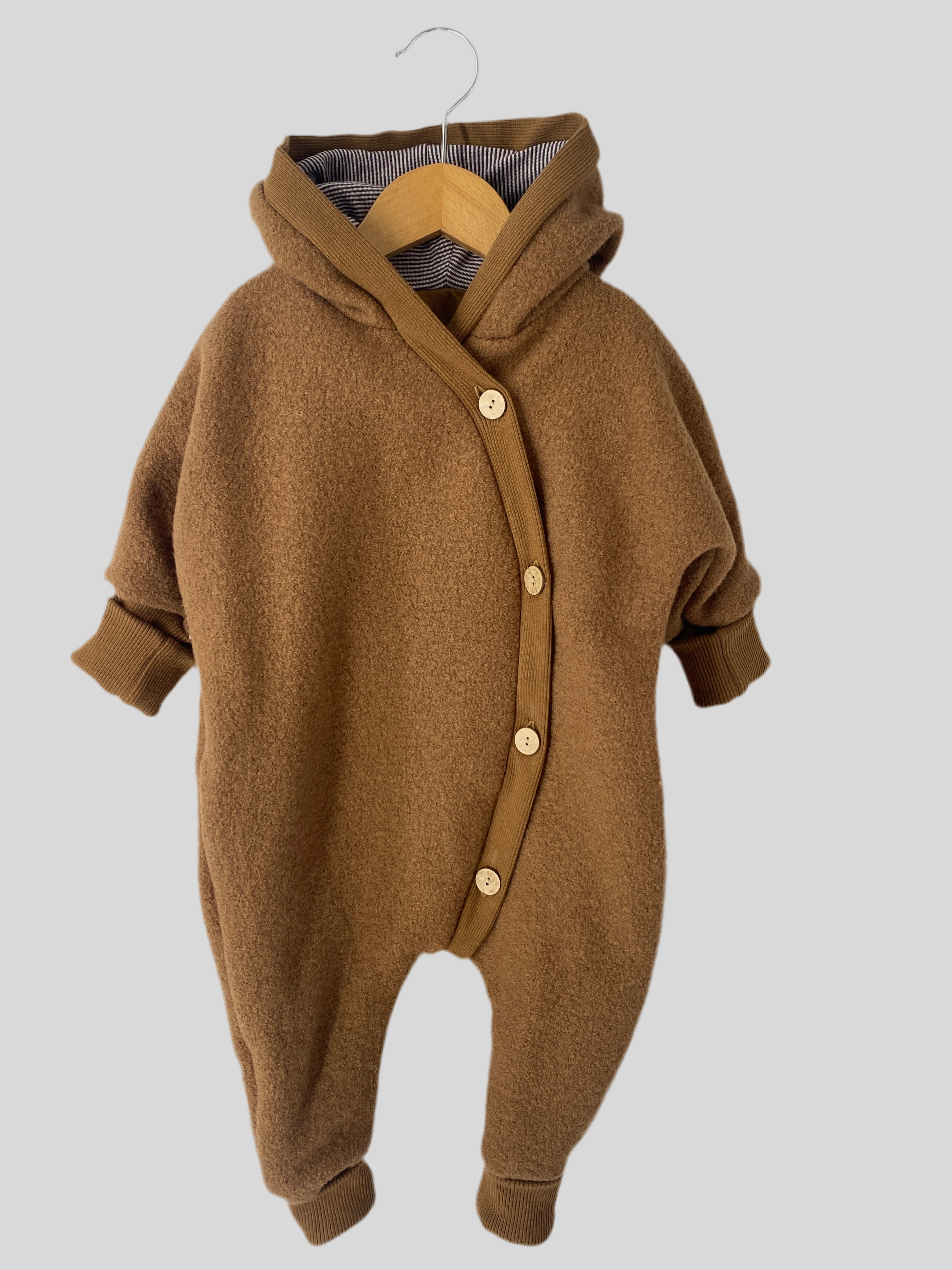 NEU Kuschelanzug Wollwalk Sahara Gr 6M: Ein brauner Baby-Romper mit gestreiftem Shirt und Knöpfen, aus weichem Material, ideal für Komfort. Begleitet von einem braunen Strickärmel und passendem Zubehör.