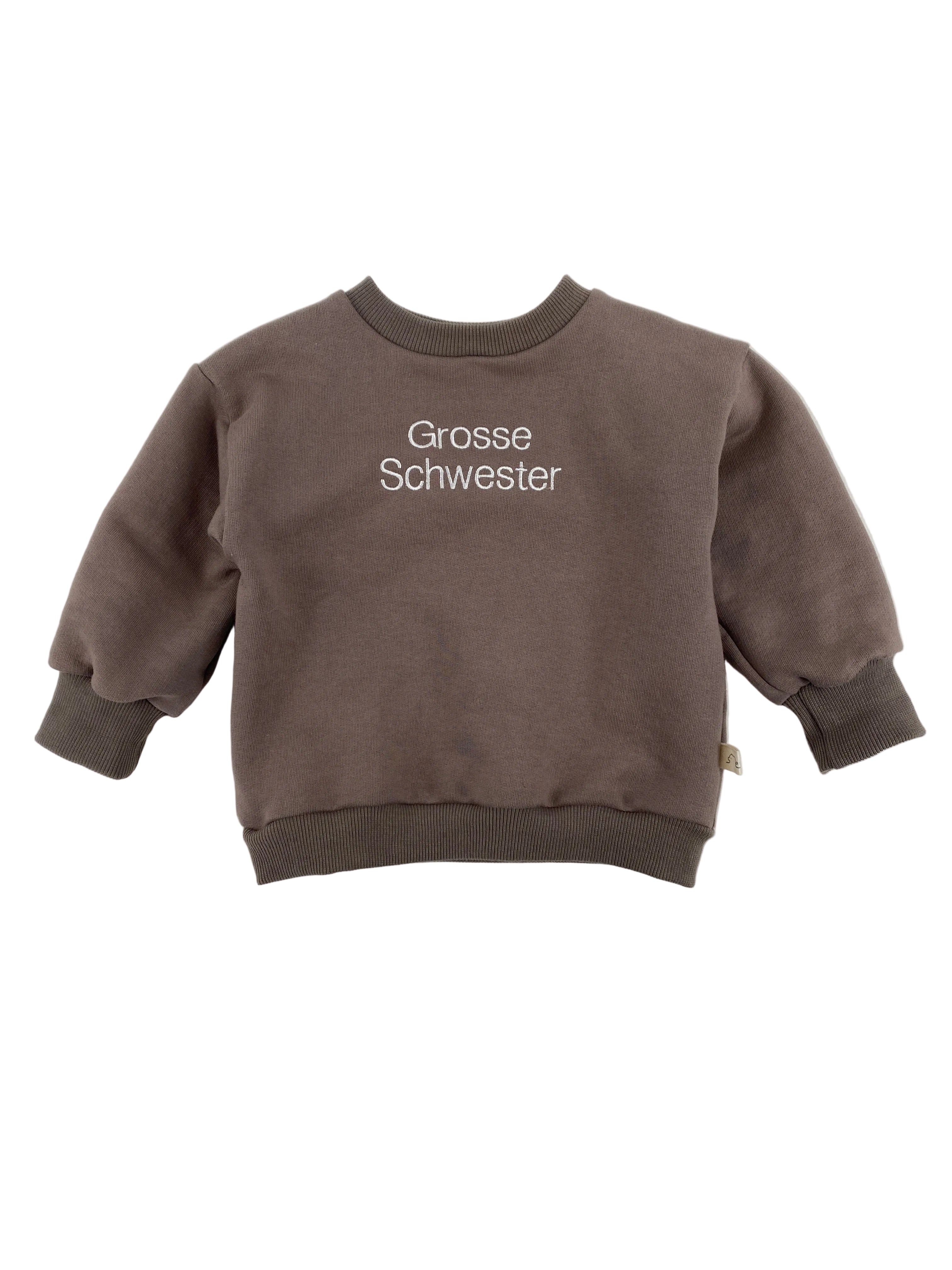 Der Pulli Bio Sweat Praline Gr 1Y zeigt einen kleinen, braunen Crewneck-Sweatshirt mit weißen Stickereien „Grosse Schwester“ vorne, ideal für Kleinkinder, mit gerippten Bündchen und Saum.