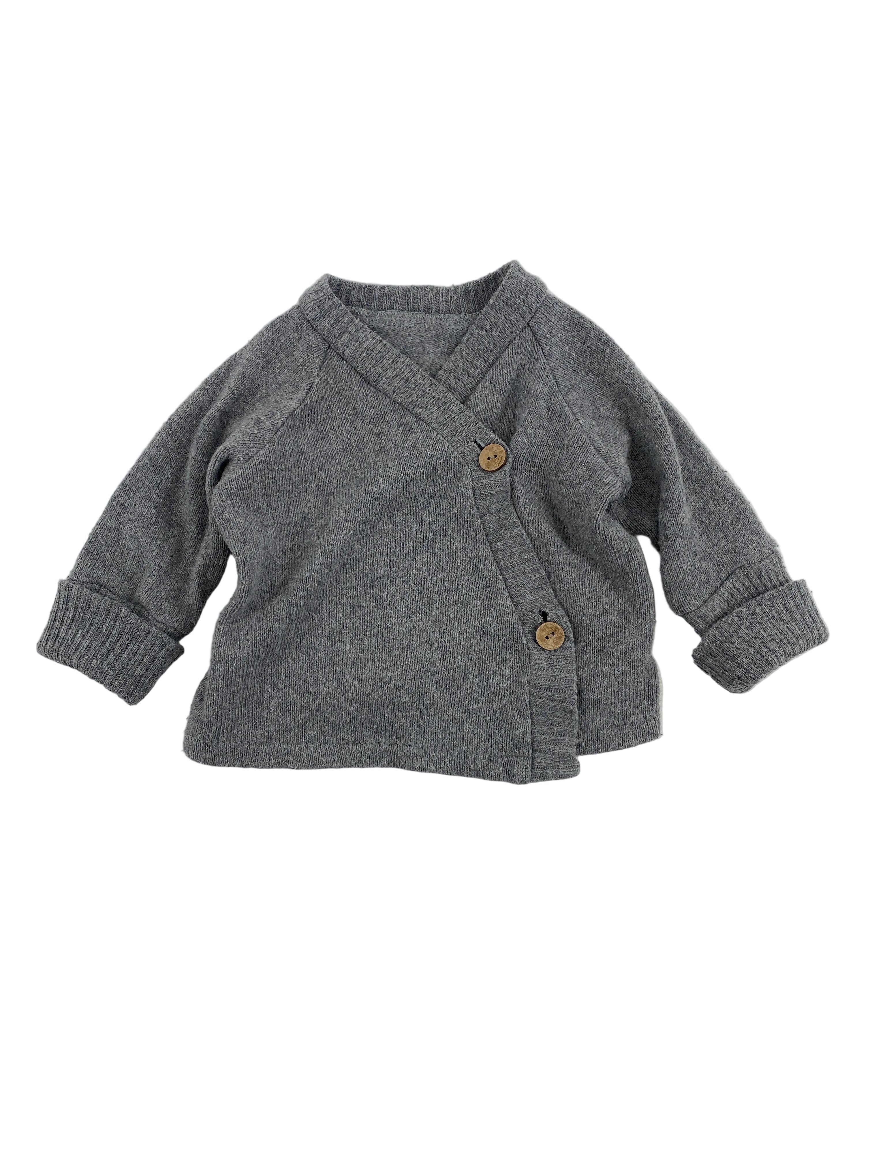 Kuschelanzug Bio Sweat Zimt Gr 3M: Kleiner, langärmeliger, grauer Strick-Cardigan im Wickelstil mit zwei Holzknöpfen an der Seite, leicht verwaschen, in gutem Zustand.
