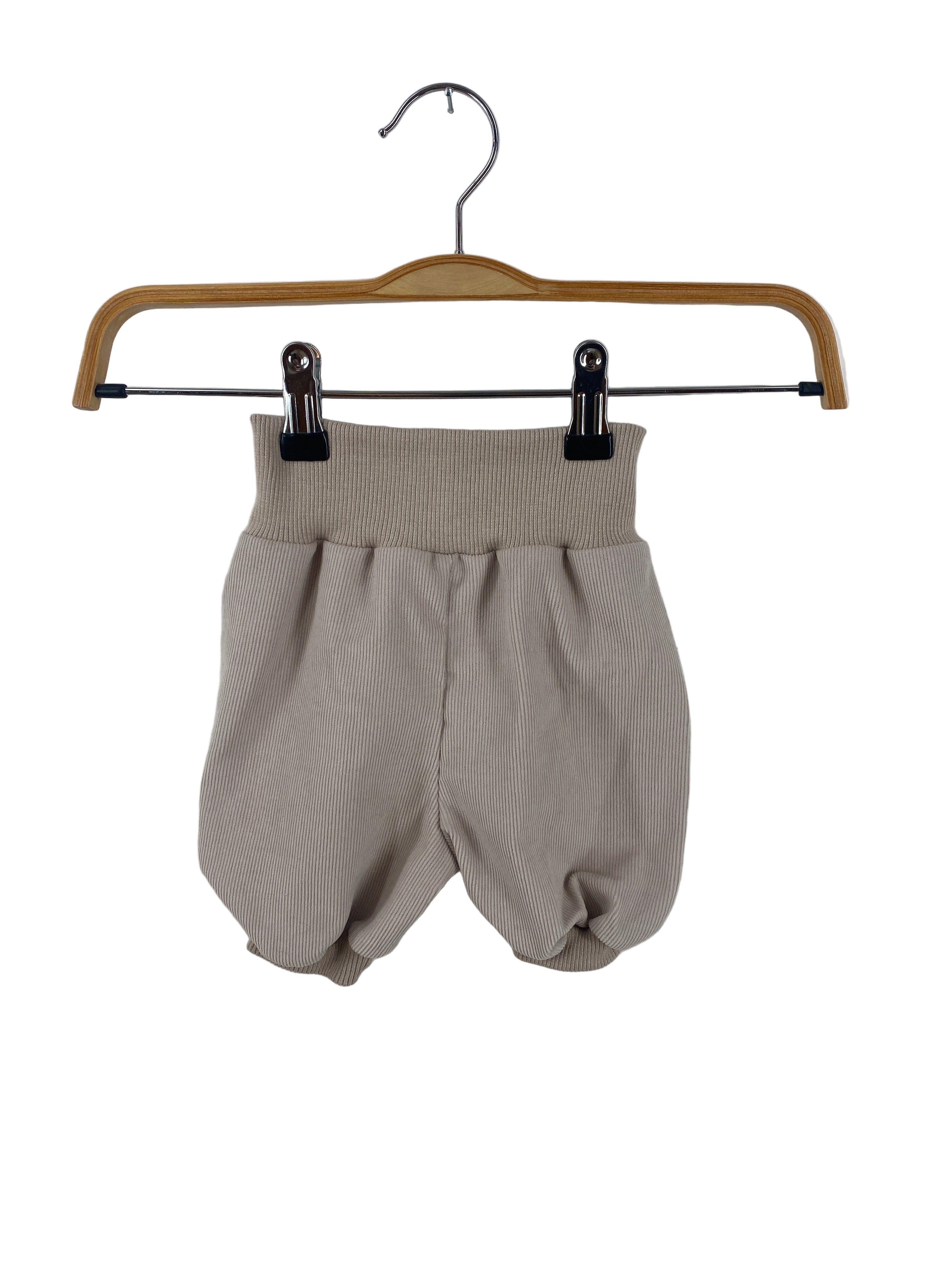 Kopie Kurze Pumphose Feincord Sand Gr 6M an einem Holzbügel, zeigt beige-taupe, gerippte Strickshorts mit hohem, dehnbarem Bund und gerundetem Beinabschluss, ideal für Babys und Kleinkinder.