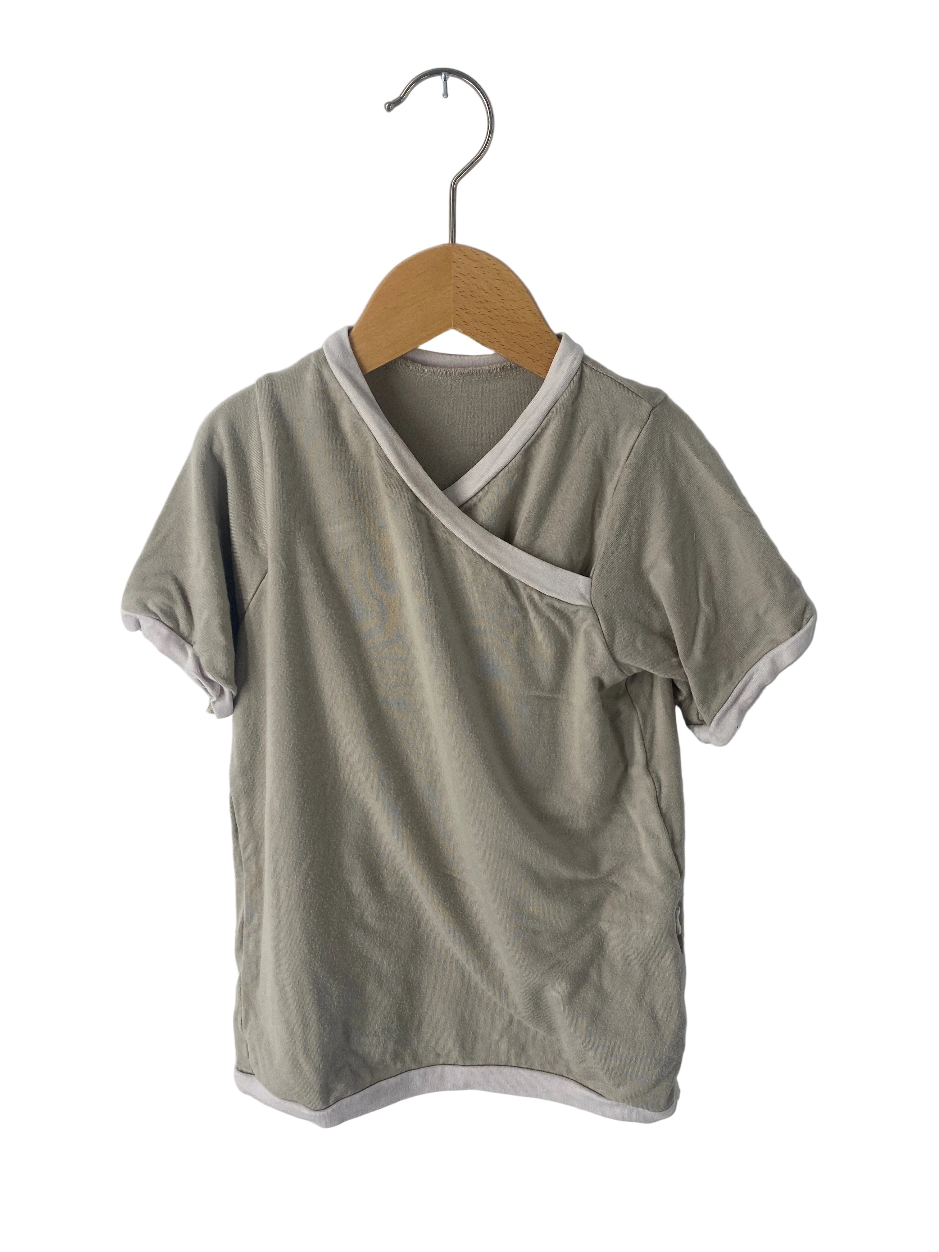 (Kopie) Ringer Shirt Bambusviskose Stein Gr 3Y: Kurzarm-Wickelshirt für Kleinkinder in gutem Zustand, präsentiert auf Holzkleiderbügel, mit cremefarbenen Abschlüssen an Kragen, Ärmeln und Saum.