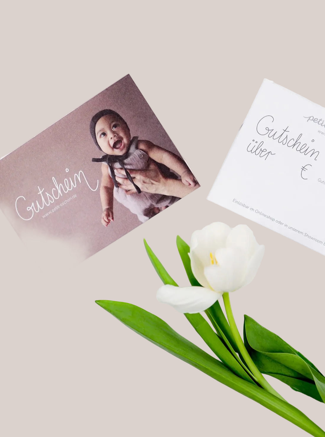 (Kopie) Geschenkgutschein: Zwei Gutscheinkarten, eine mit lächelndem Baby, eine zum Ausfüllen, neben einer weißen Tulpe. Einlösbar online und in Berlin-Tempelhof.