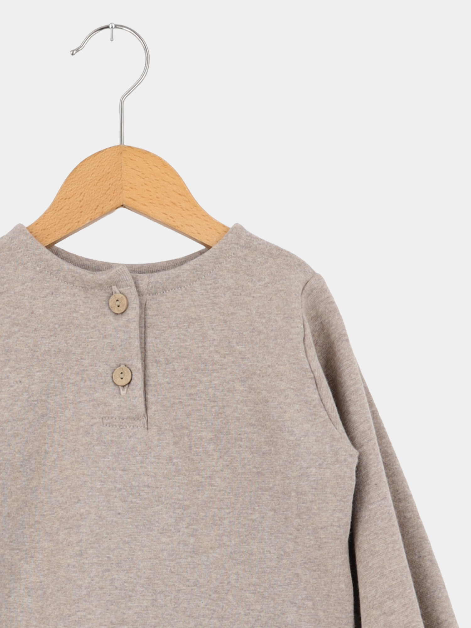 Hemdchen Feinstrick - Hafer: Langärmliges, heather-taupefarbenes Pullover-Top mit rundem Ausschnitt und kurzer Knopfleiste, auf einem Holzkleiderbügel hängend. Ideal für Babys und Kleinkinder, weich und dehnbar.