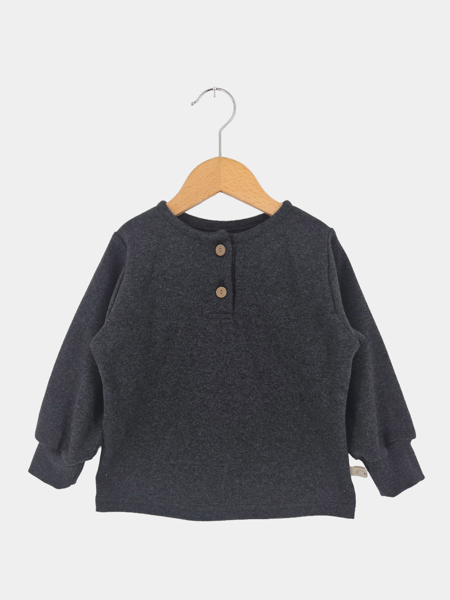 Hemdchen Feinstrick - Ruß: Ein langärmeliges Henley-Shirt für Kinder, aus weichem Feinstrick mit rundem Ausschnitt und zwei Holzknöpfen, auf einem Holzbügel vor weißem Hintergrund.