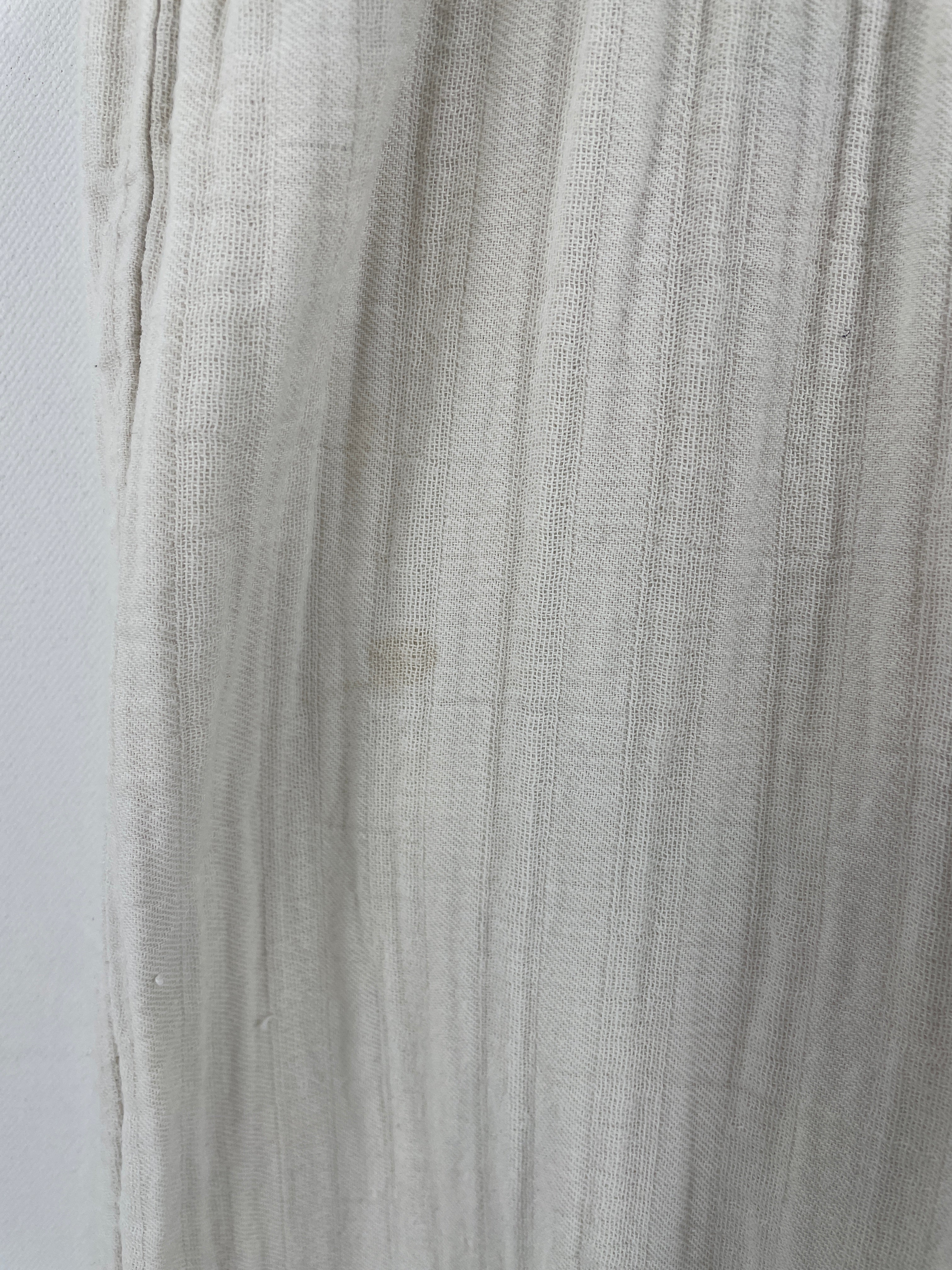 Nahaufnahme eines Damen Jumpsuits Musselin Natur Gr. S mit locker gewebtem Stoff und vertikaler Streifenstruktur. Ein kleiner Fleck ist vorne sichtbar. Der Jumpsuit hat praktische Handtaschen.