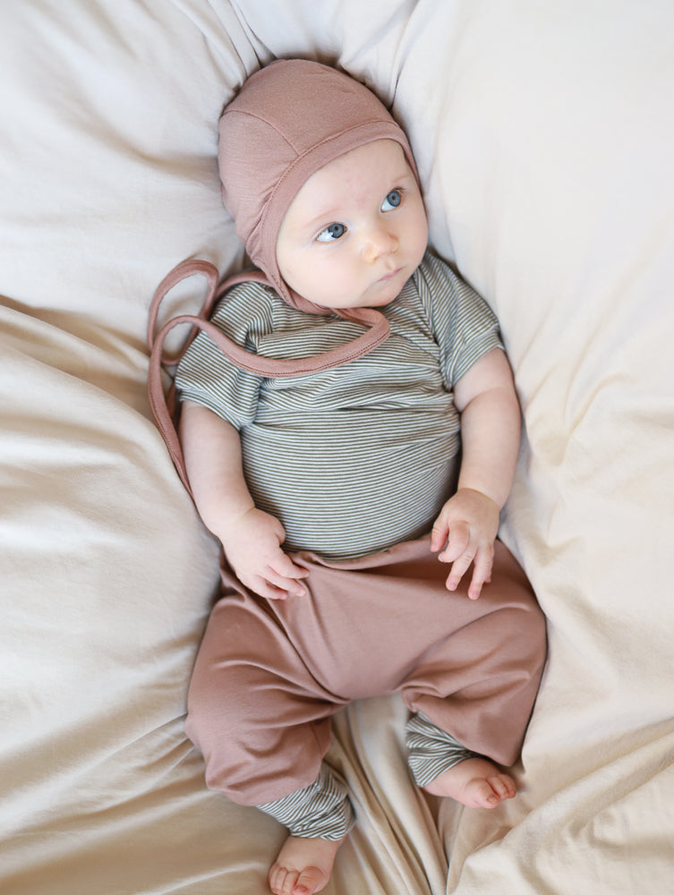 Babyknicker Jersey - Puder: Ein Baby trägt eine staubrosa Strickmütze, gestreiften Body und passende weiche Hose. Die Babyknicker bietet Bewegungsfreiheit und Komfort, ideal für empfindliche Haut.