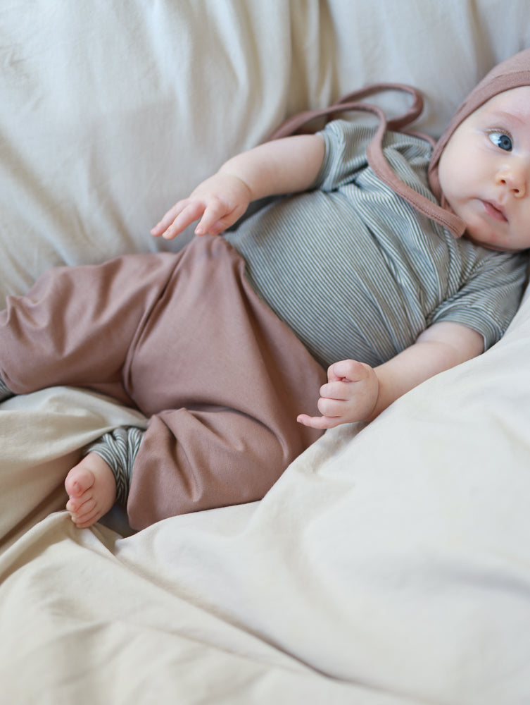 Babyknicker Jersey - Puder: Ein Baby trägt eine gestreifte Kurzarm-Body mit lockeren, puderfarbenen Jersey-Hosen aus 100% Bio-Baumwolle, die viel Bewegungsfreiheit bieten.