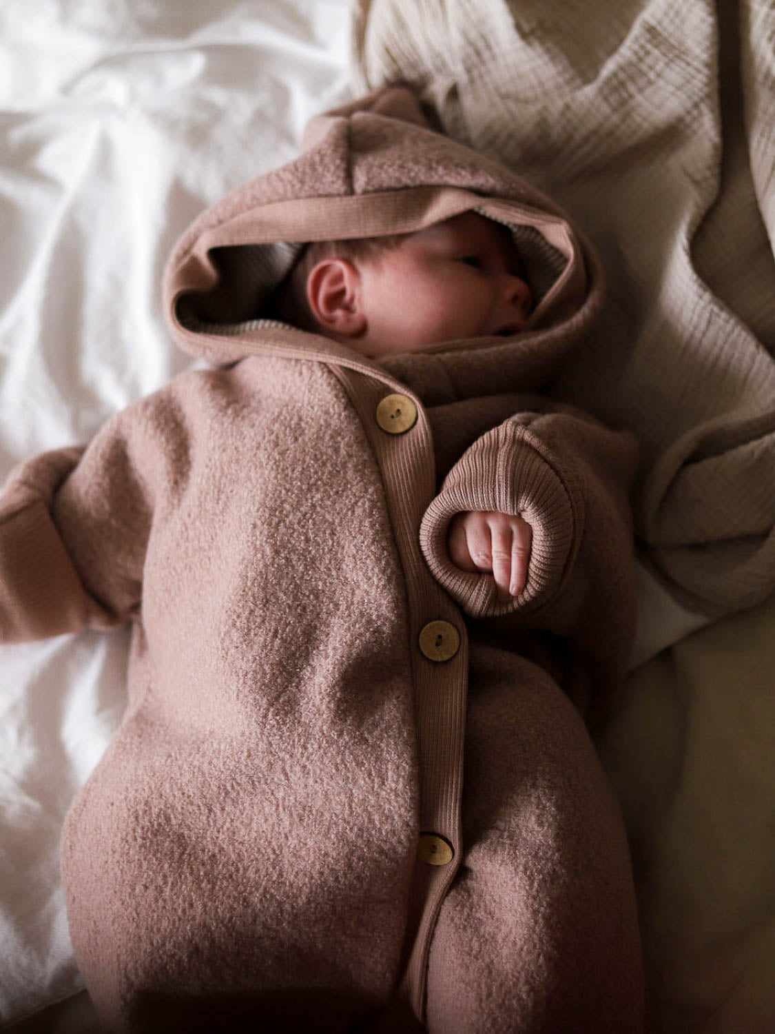 Ein Baby schläft in einem Kuschelanzug Wollwalk - Puder, aus 100% Schurwolle mit Bio-Jersey-Futter, ideal für kühle Jahreszeiten.