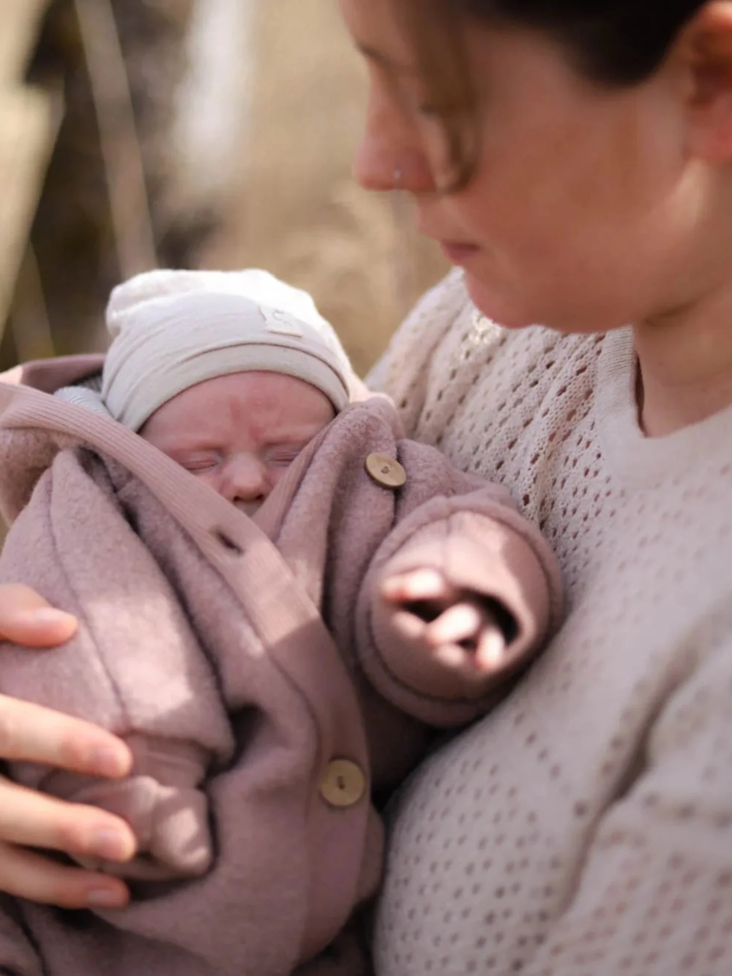 Erwachsener hält Baby in Kuschelanzug Wollwalk - Puder, aus Schurwolle mit Baumwollfutter, großzügig geschnitten, mit umklappbaren Bündchen, ideal für kühlere Tage.