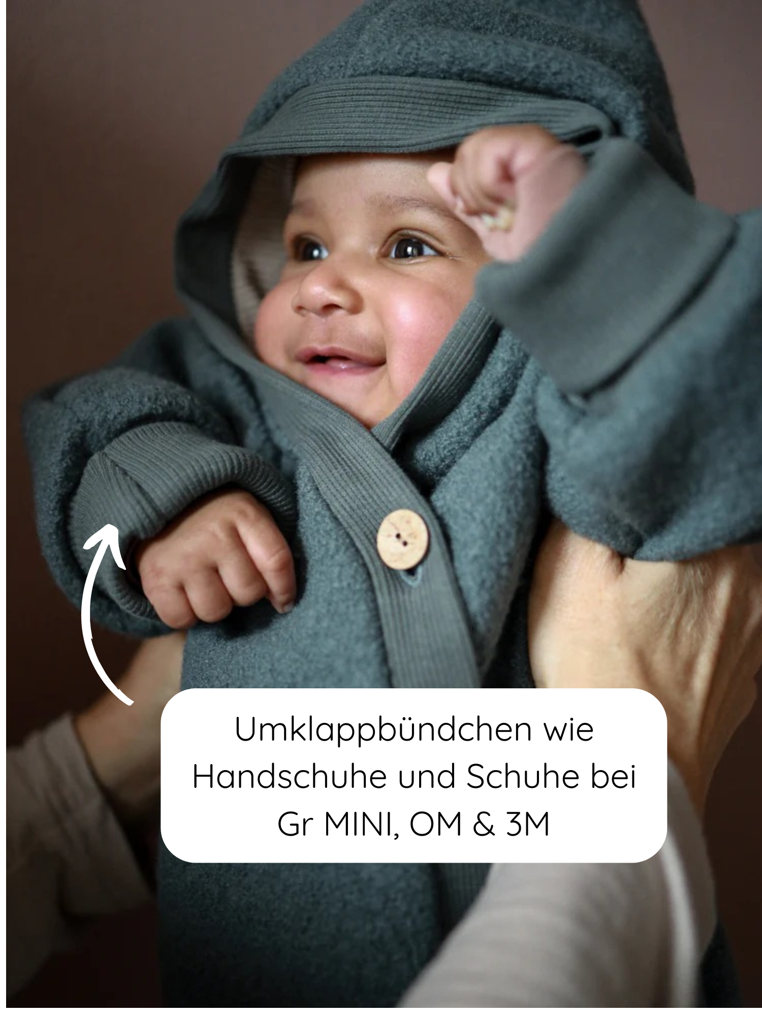 Ein lächelndes Baby trägt den Kuschelanzug Wollwalk - Taube, mit einer umklappbaren Ärmelmanschette als Fäustling. Wollwalk Overall für Babys und Kinder in Taube